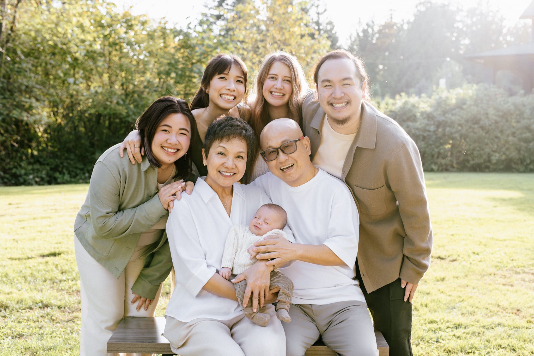 Outdoor family portrait photography of three generations hugging on the grass around grandparents holding a newborn