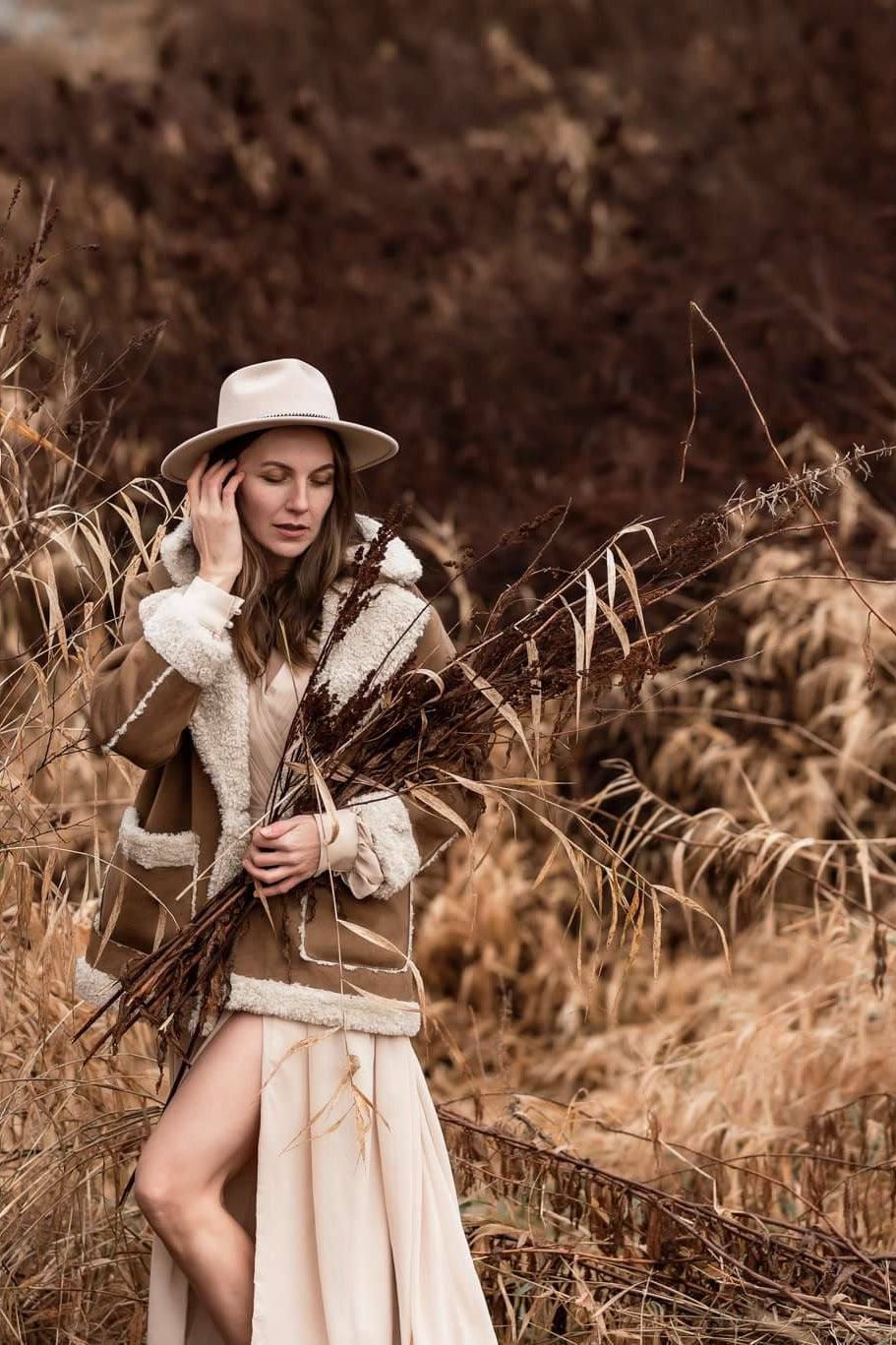 Creative portrait photography in tall golden grass, woman in a hat and fringed jacket