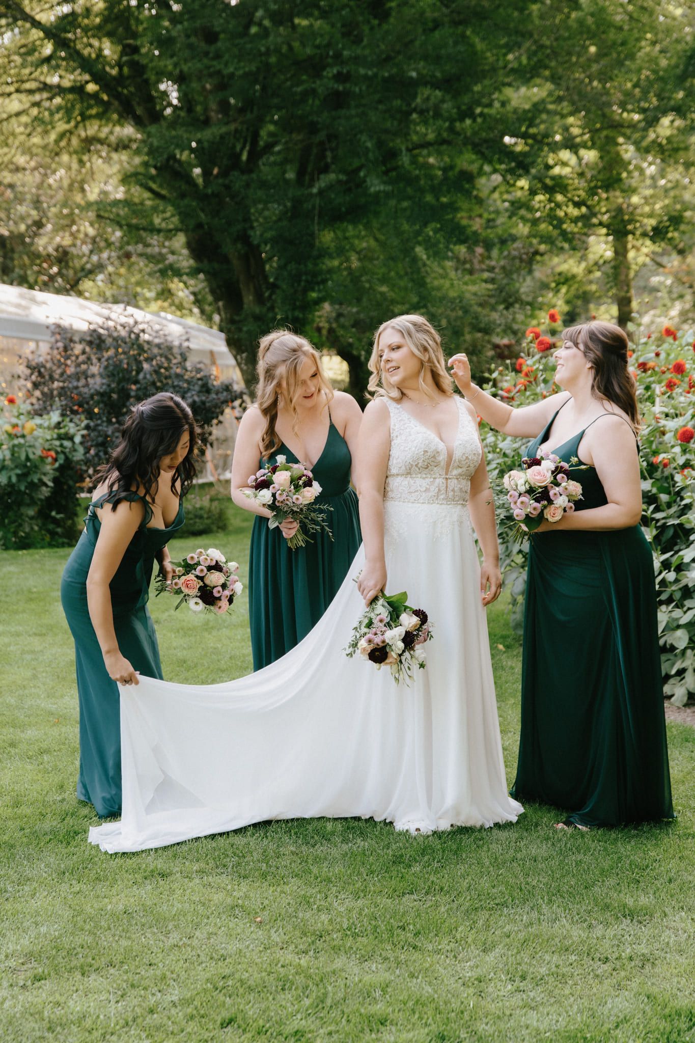 Wedding gown photoshoot on the lawn, bridesmaids in green arranging the bride's train