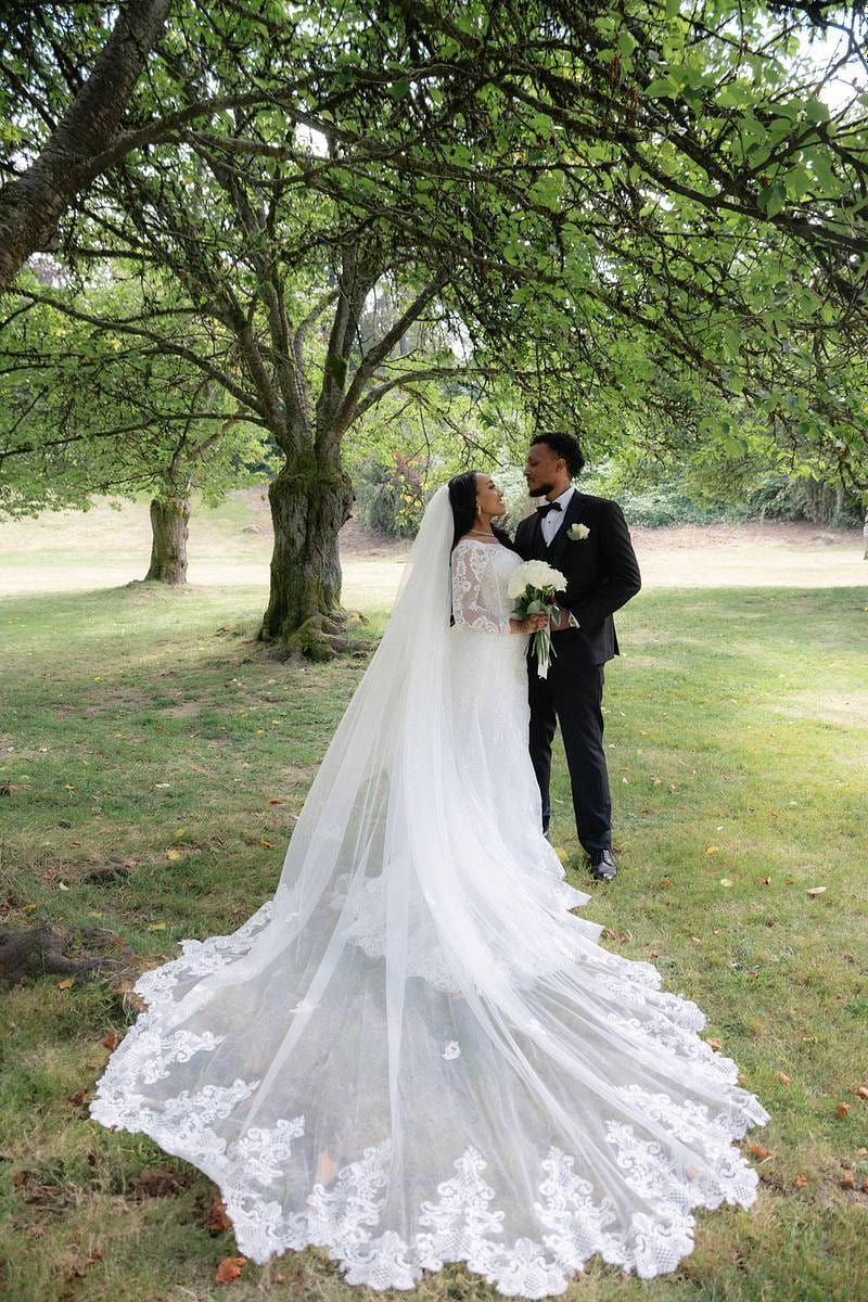 Wedding gown photos across the grass, bride and groom kissing under a tree, her lace train spread