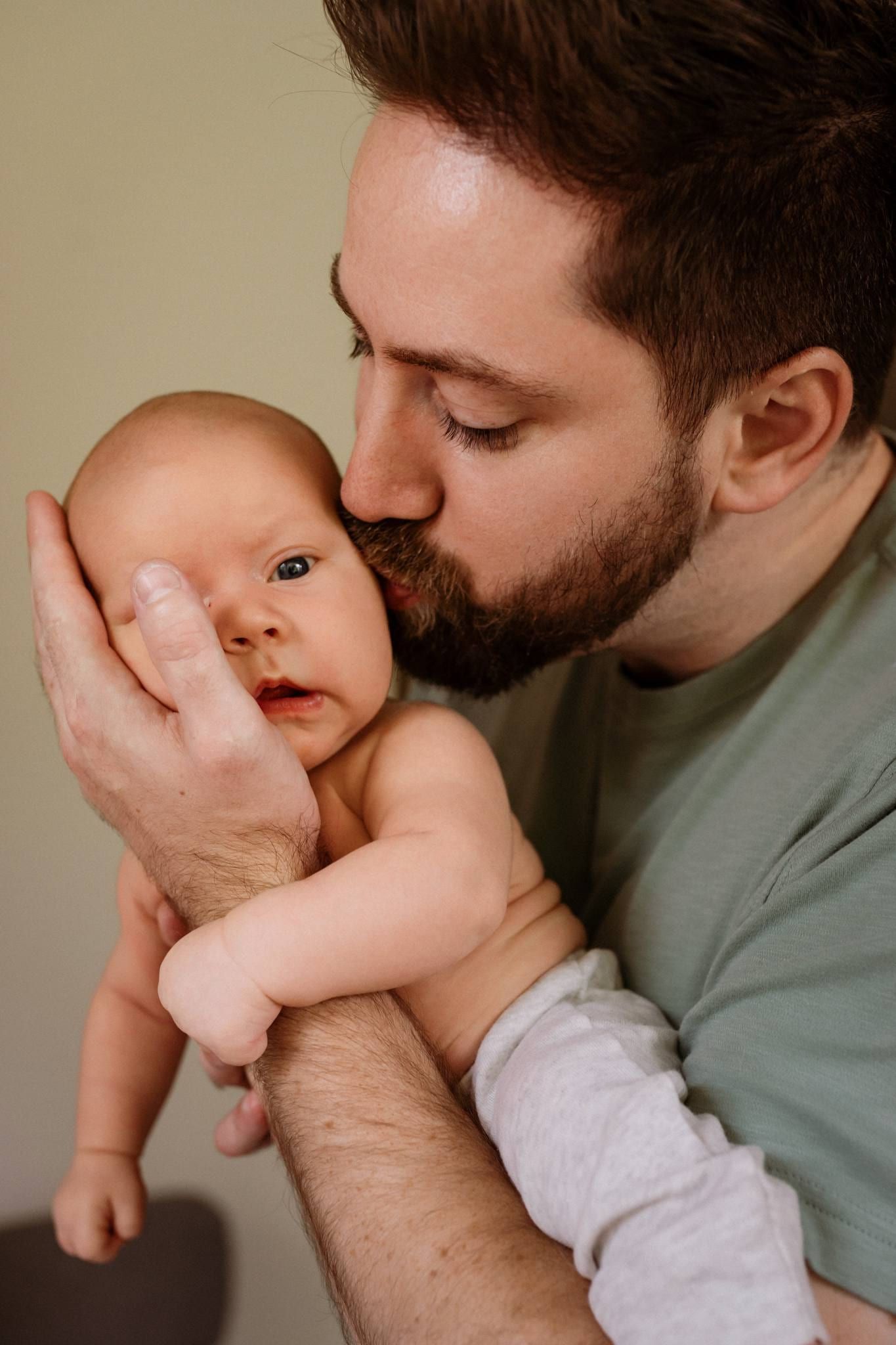 Father kissing his wide-eyed newborn's head