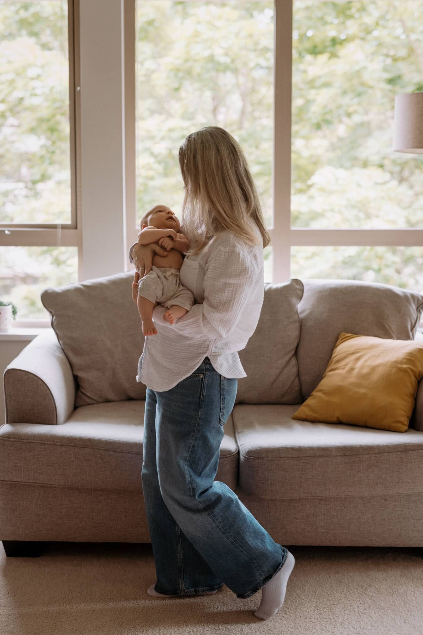 Mother standing by the window rocking her newborn in a sunlit living room