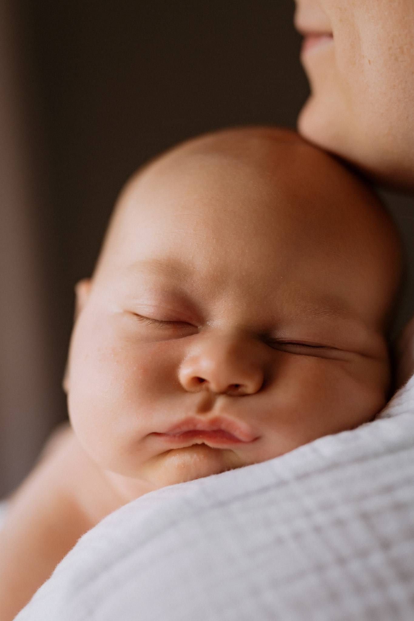 Close-up of a sleeping newborn's face resting on a parent's shoulder