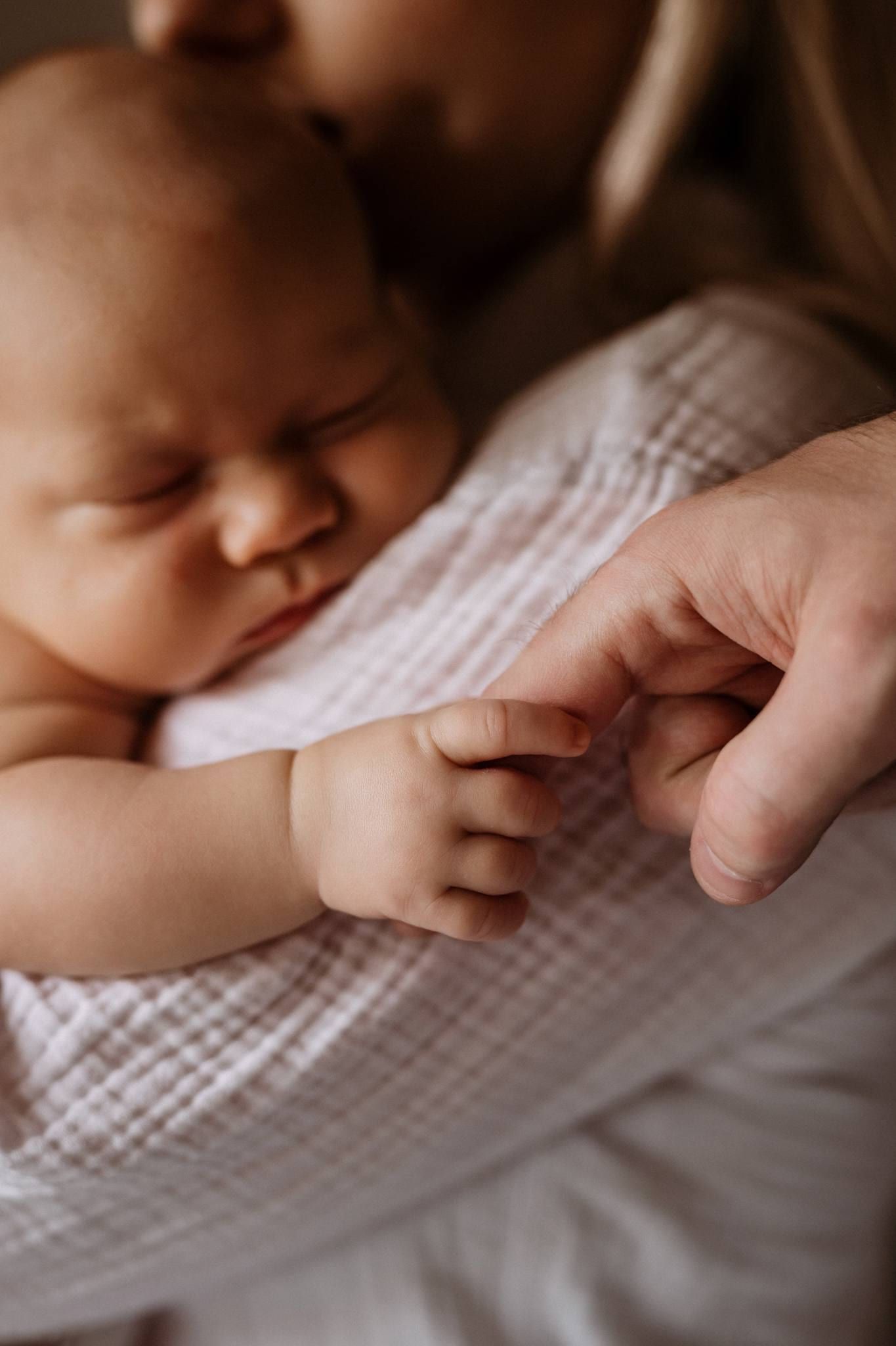 Sleeping newborn's tiny fingers wrapped around a parent's thumb