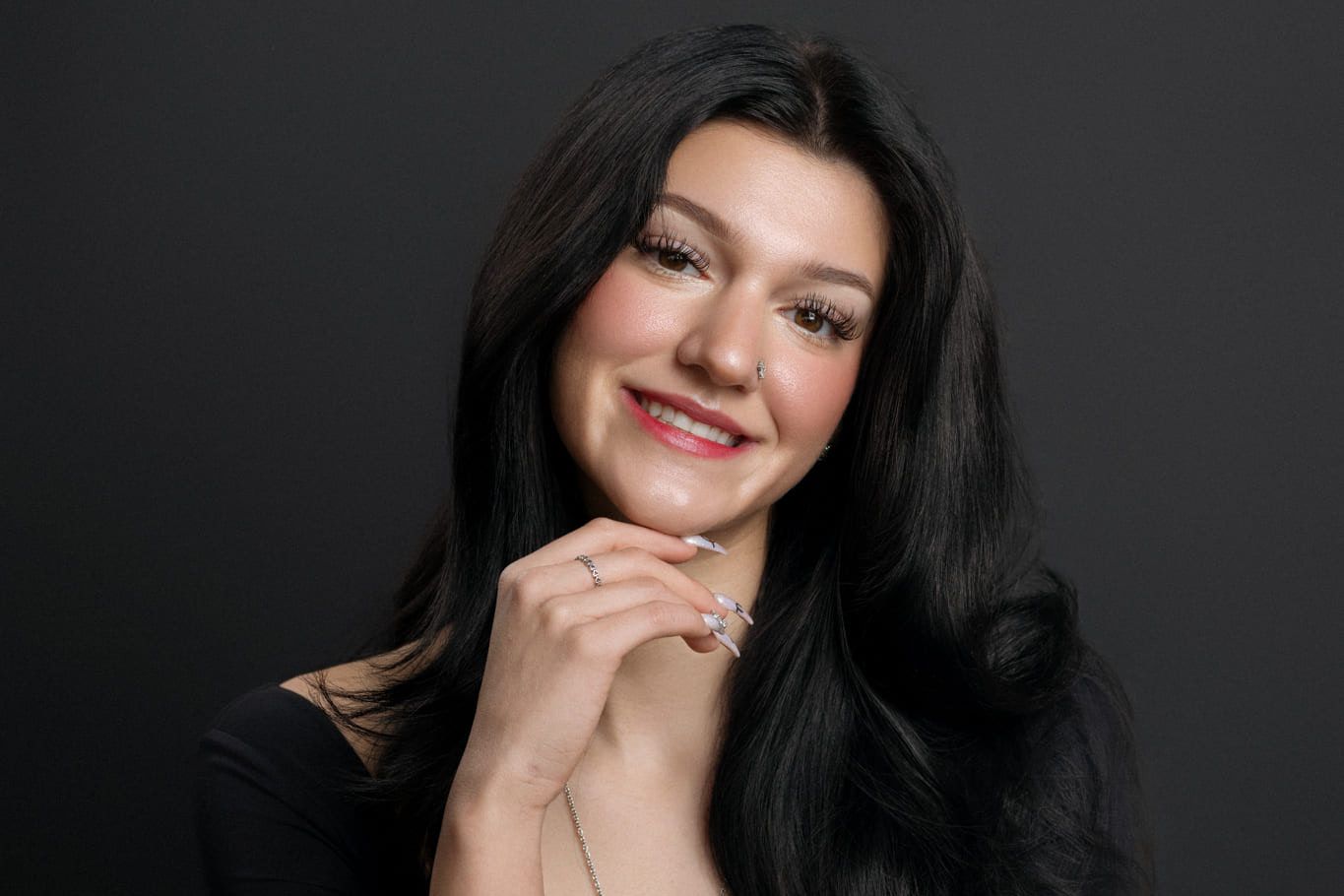 Corporate photoshoot, smiling young woman with long dark hair resting her chin on her hand