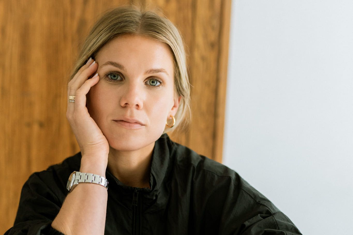 Professional business portrait photography, blonde woman in a dark jacket resting her cheek on her hand