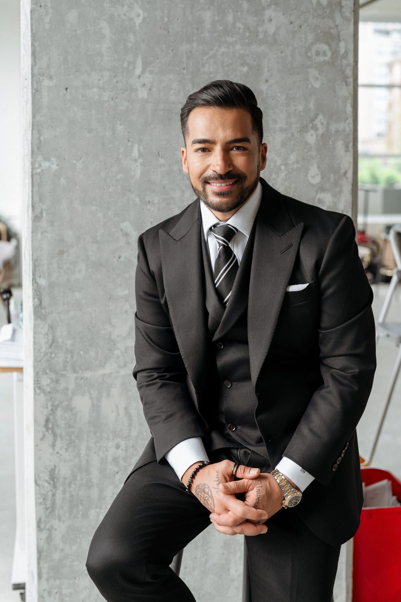 Headshot image, man in a pinstriped suit sitting against a concrete column