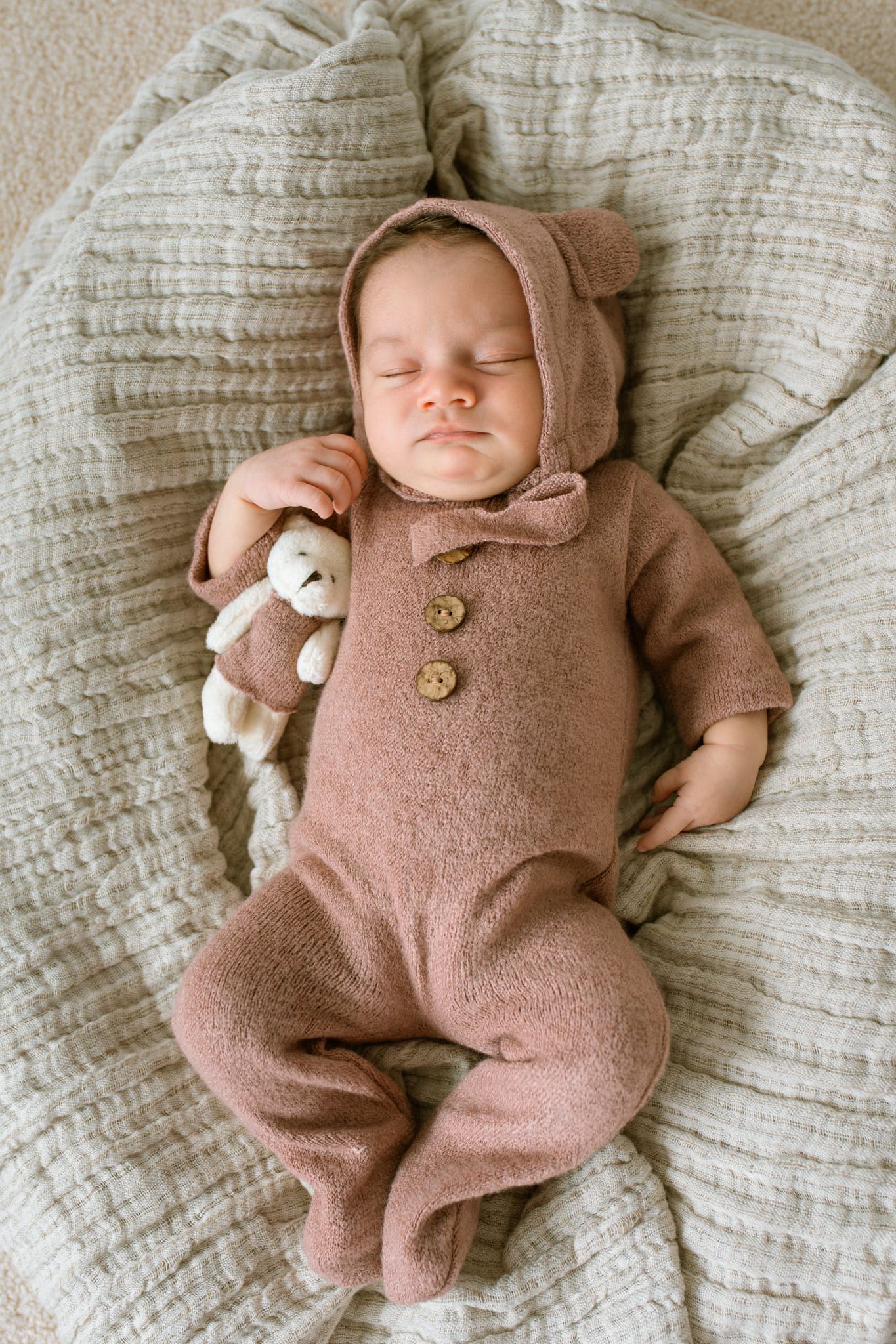 Indoor newborn photos at home, newborn in a pink knit romper and bear hood