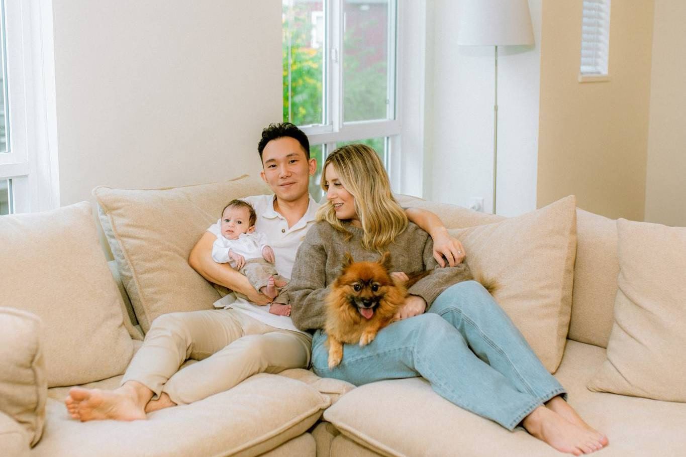 Newborn photos at home, parents with their newborn and their Pomeranian on a cream sofa