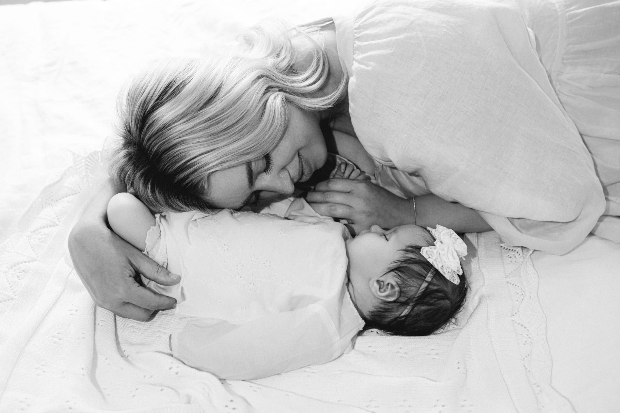 Lifestyle newborn shoot, mom lying face to face with her newborn on the bed, in black and white