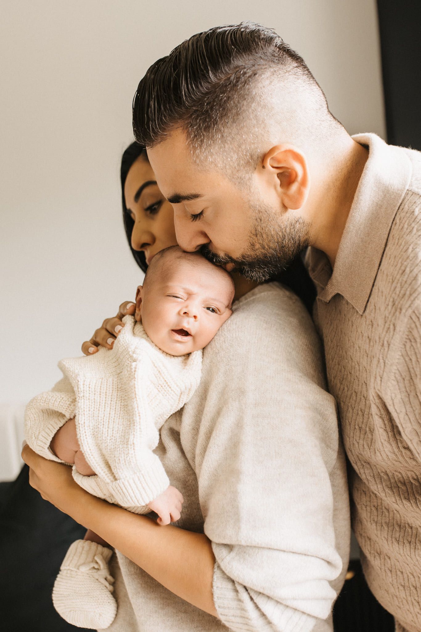 Newborn photos in Coquitlam, newborn in a cream knit outfit with his parents at home