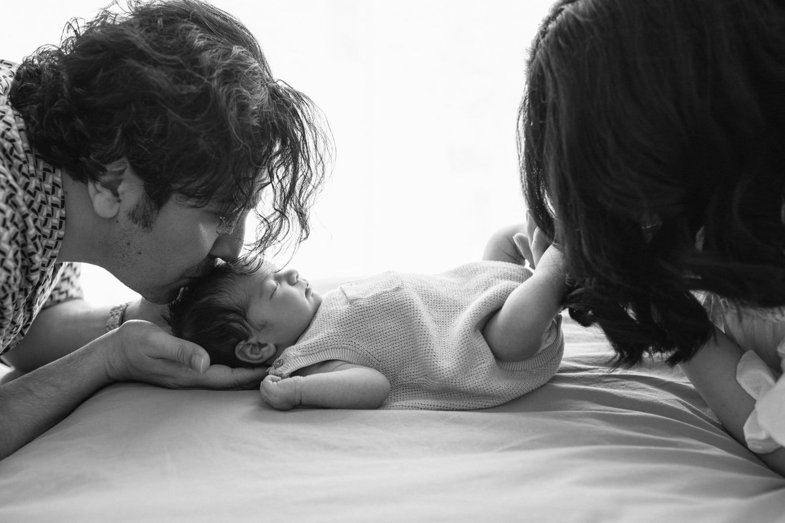Newborn at home photoshoot on the bed, dad kissing the newborn, in black and white