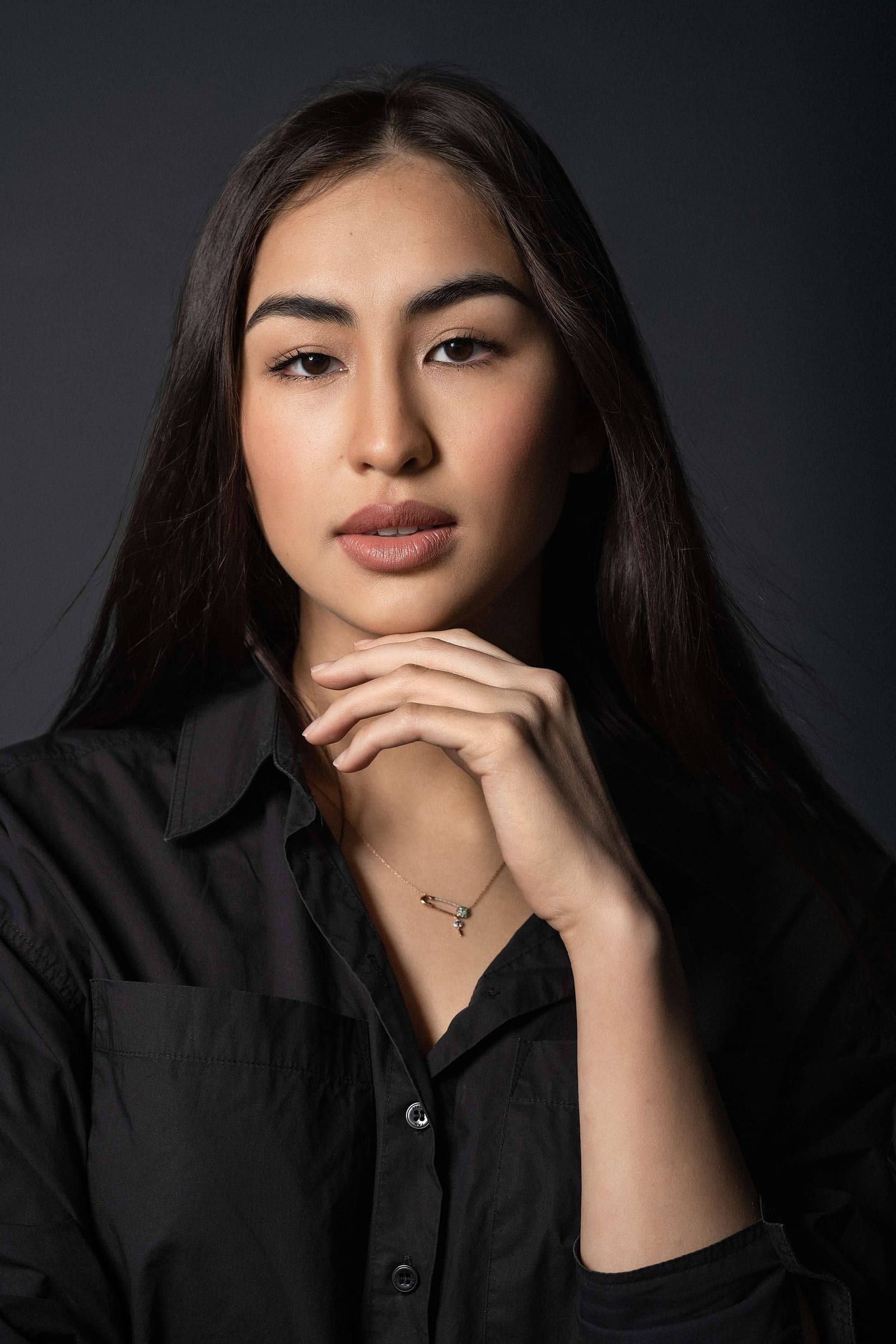 Studio headshot of a woman in a black shirt, hand at her chin, on a dark backdrop
