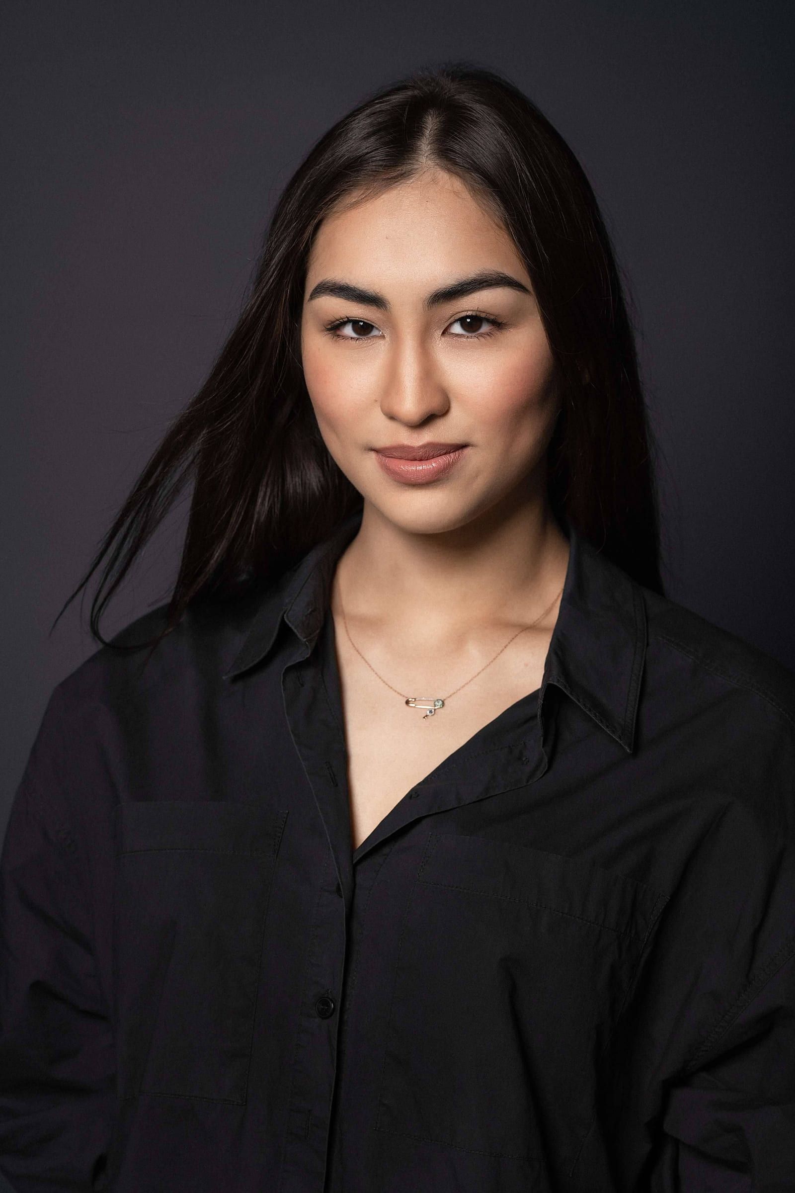 Woman with long dark hair in a black shirt on a dark backdrop