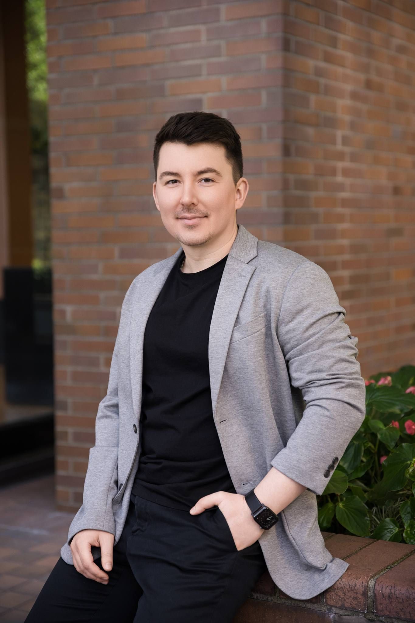 Man in a grey blazer seated on a brick wall outdoors