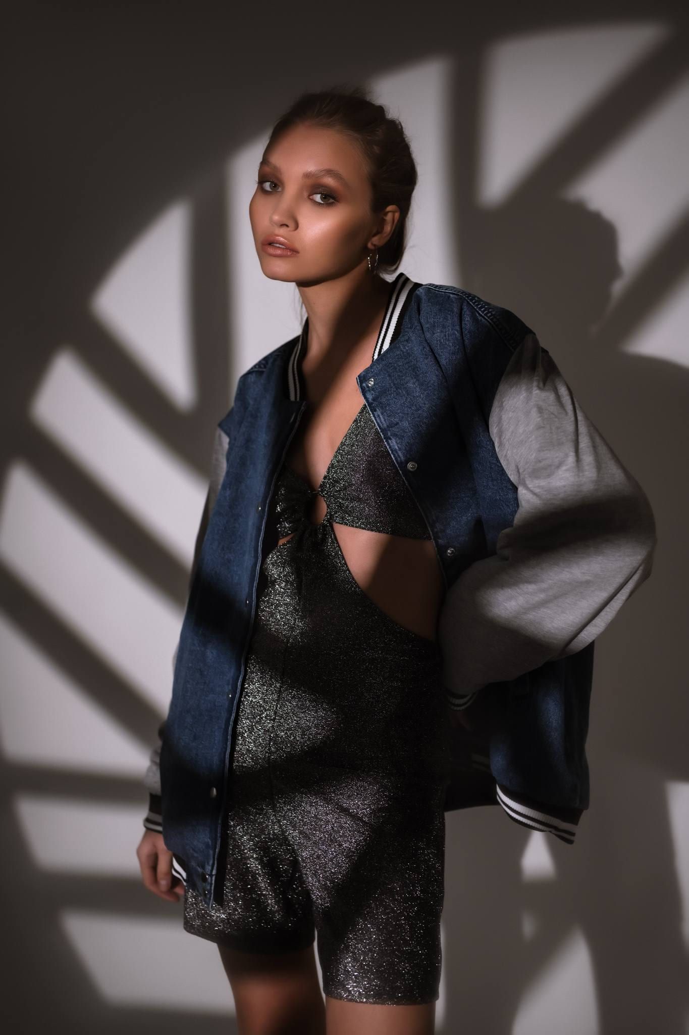 Model in a blue bomber jacket under palm-leaf shadows