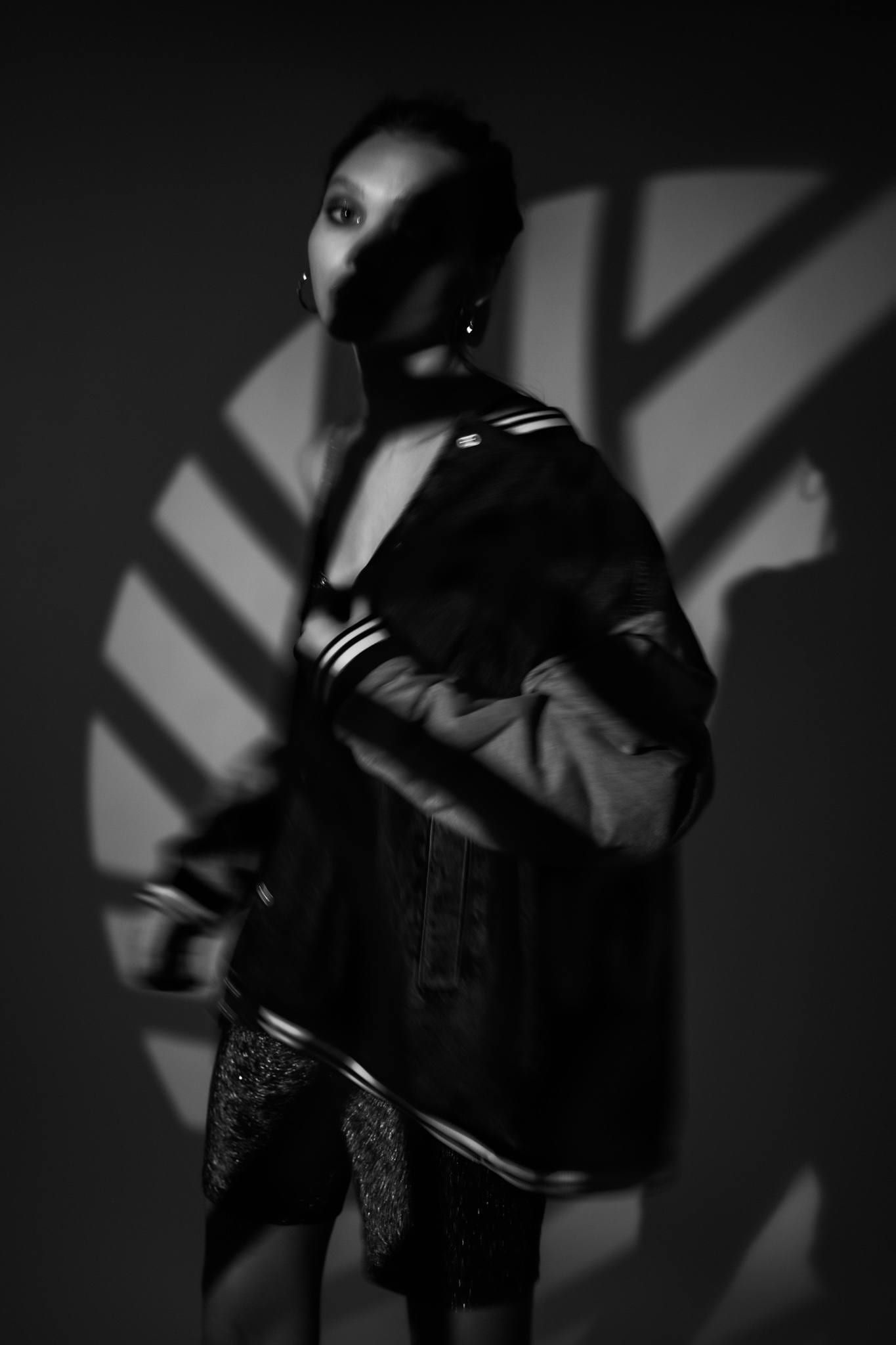 Black-and-white photo of a model in a bomber jacket under leaf shadows