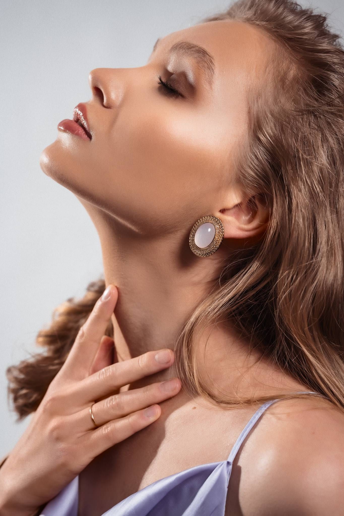 Beauty profile of a blonde model in a lilac top, hand on her neck