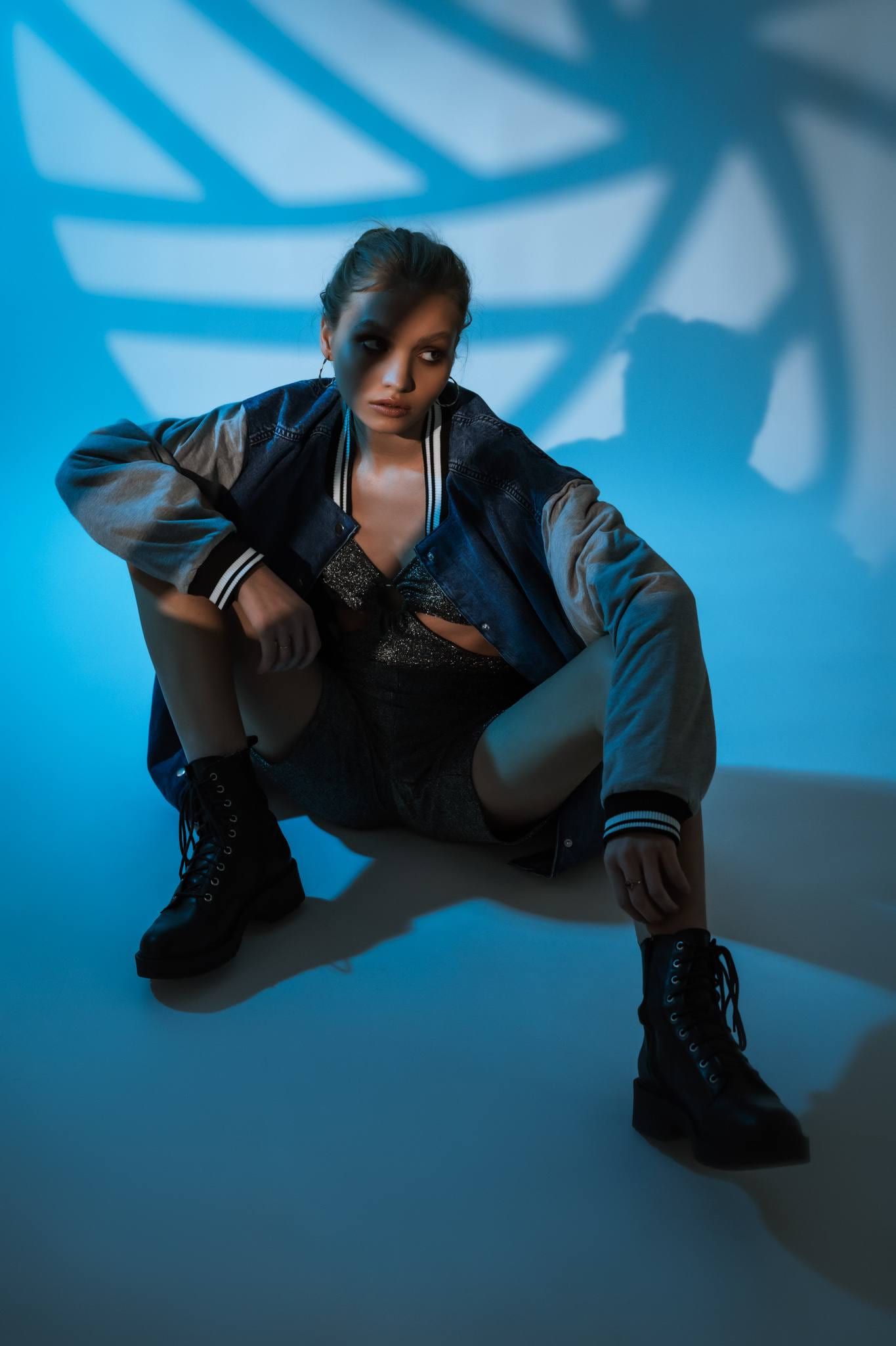 Model crouched in a bomber jacket under blue-and-white patterned light