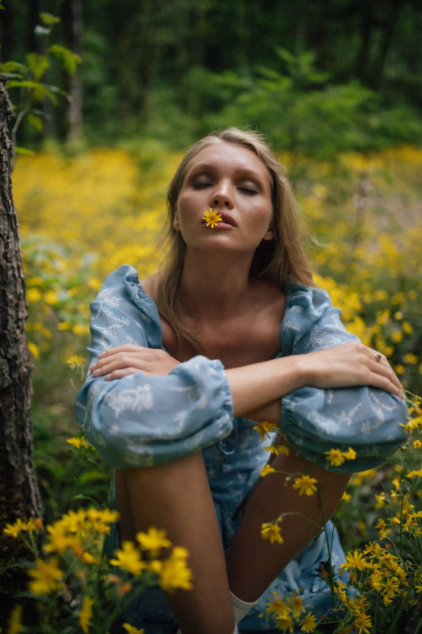 Model in a blue floral dress with arms crossed in a field of yellow flowers