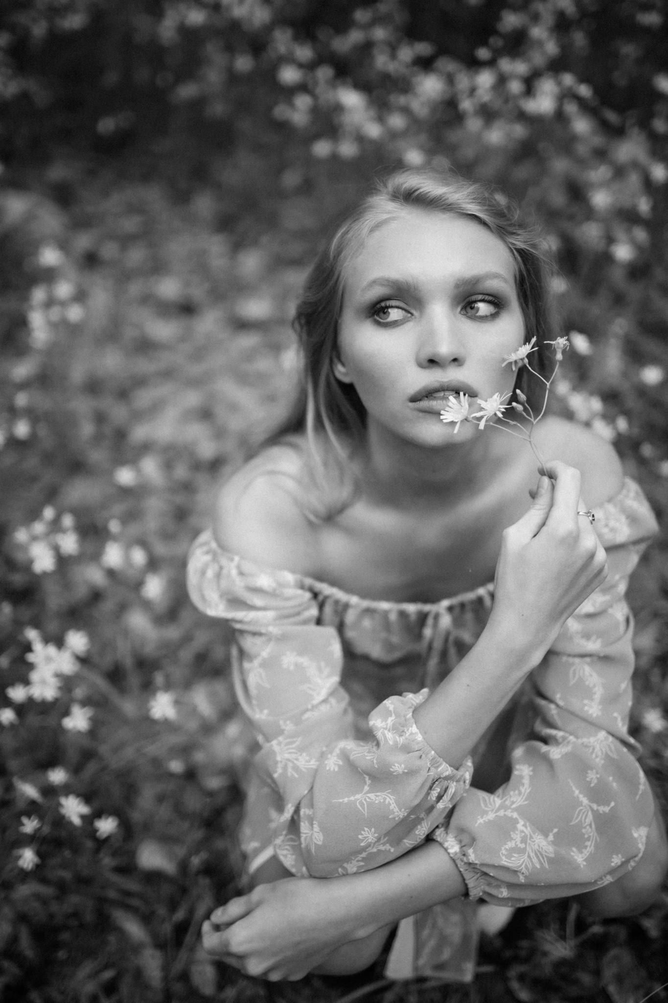Black-and-white portrait of a model in a floral dress with arms crossed among flowers
