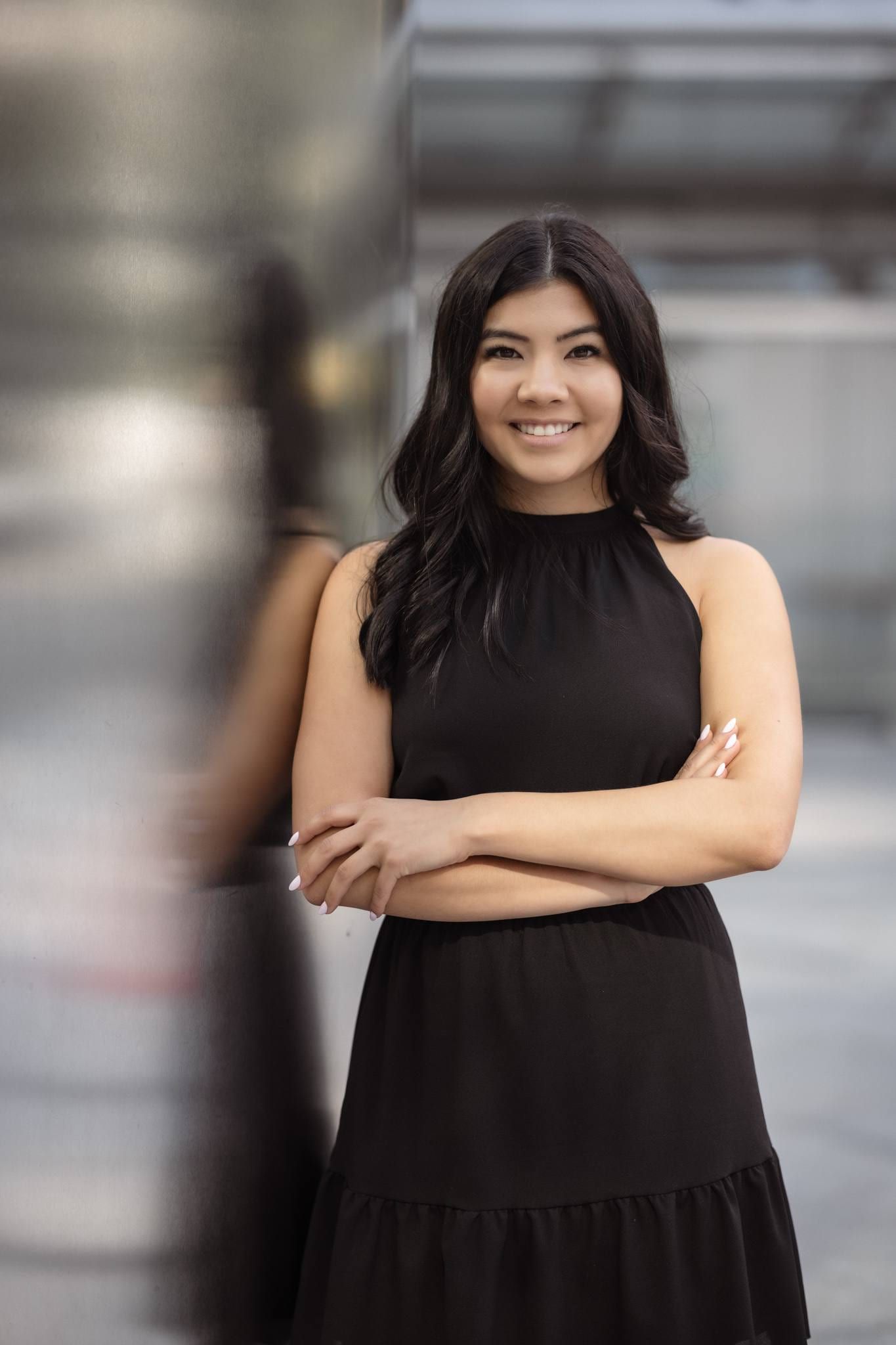 Woman in a black dress with arms crossed outside a downtown building