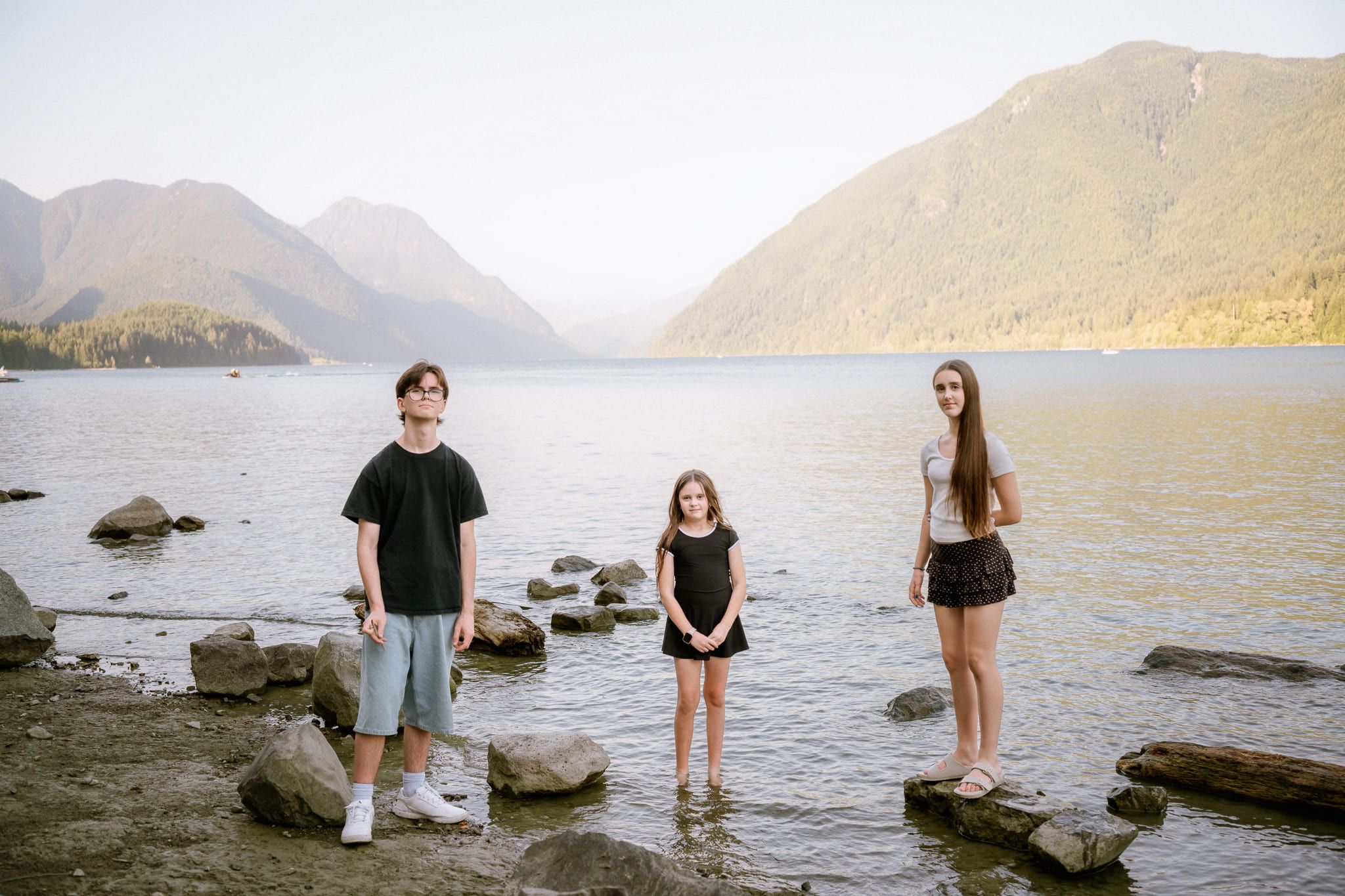 Family outdoor shoot of three kids standing on the stones of a mountain lake