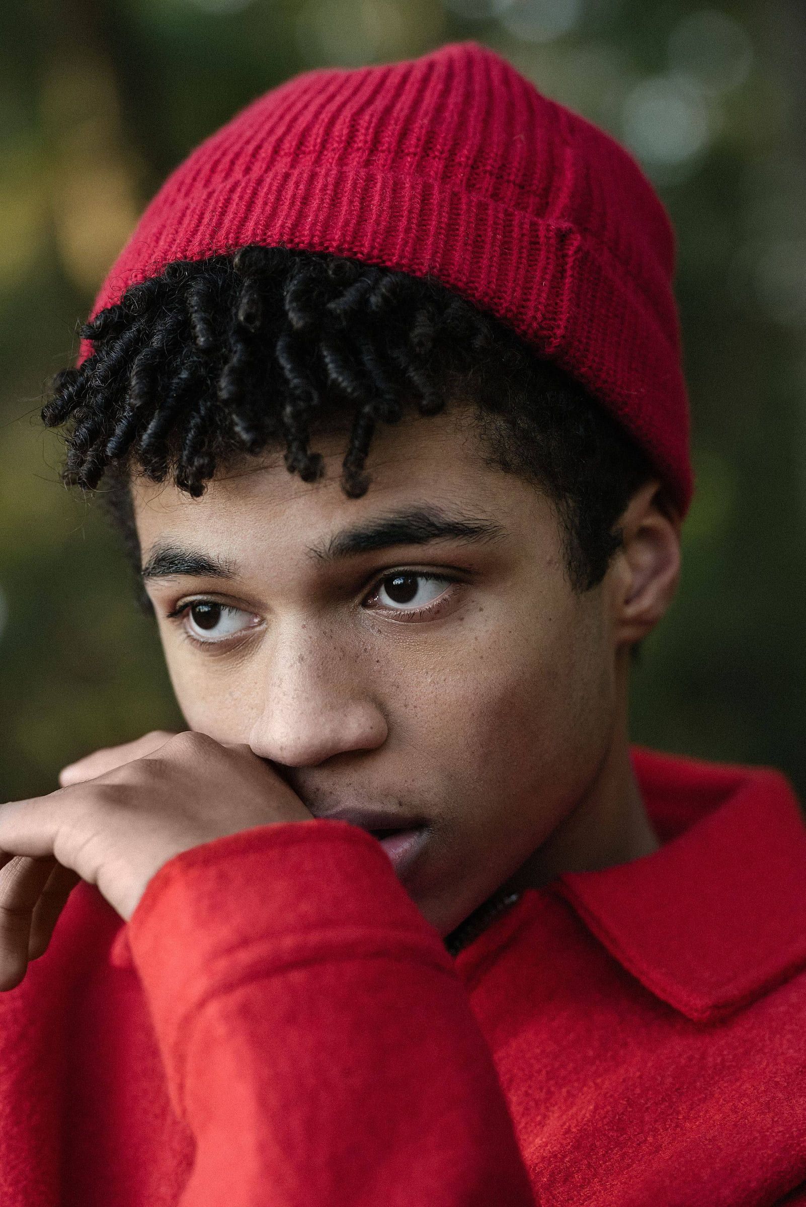 Young man in a red beanie and red sweater, hand at his chin
