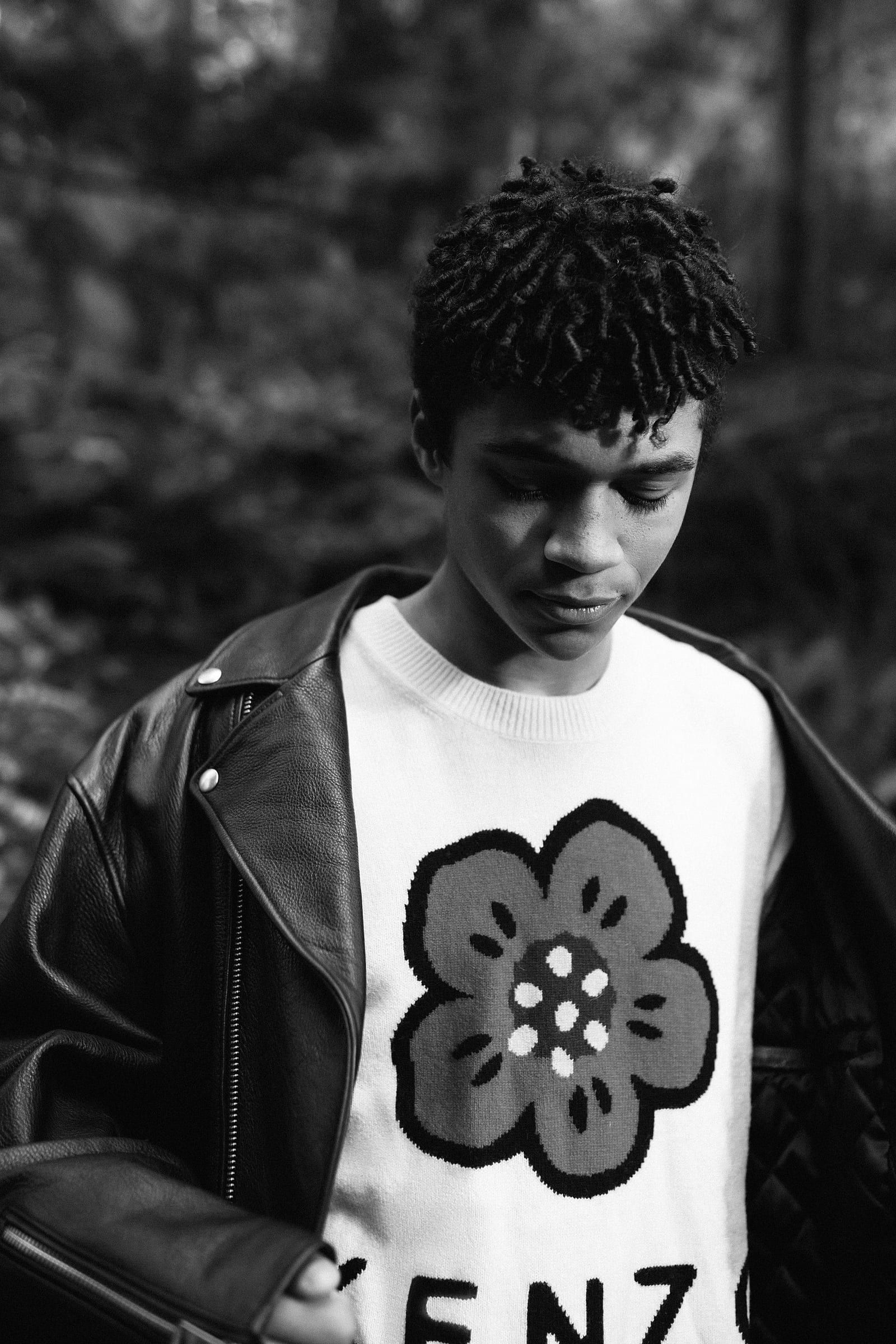 Young man in a graphic tee and leather jacket, a hand at his face