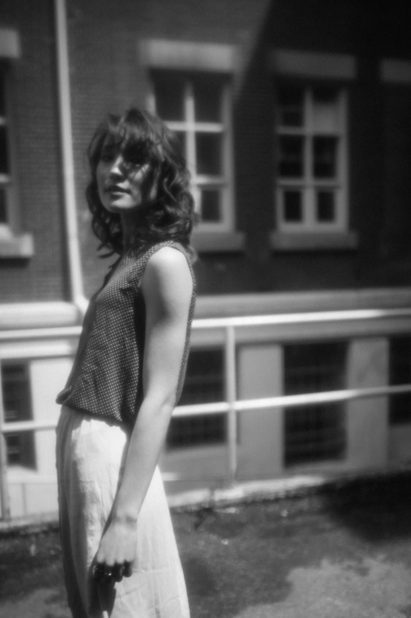 Black-and-white photo of a model in a striped skirt and tank top by a stairwell railing