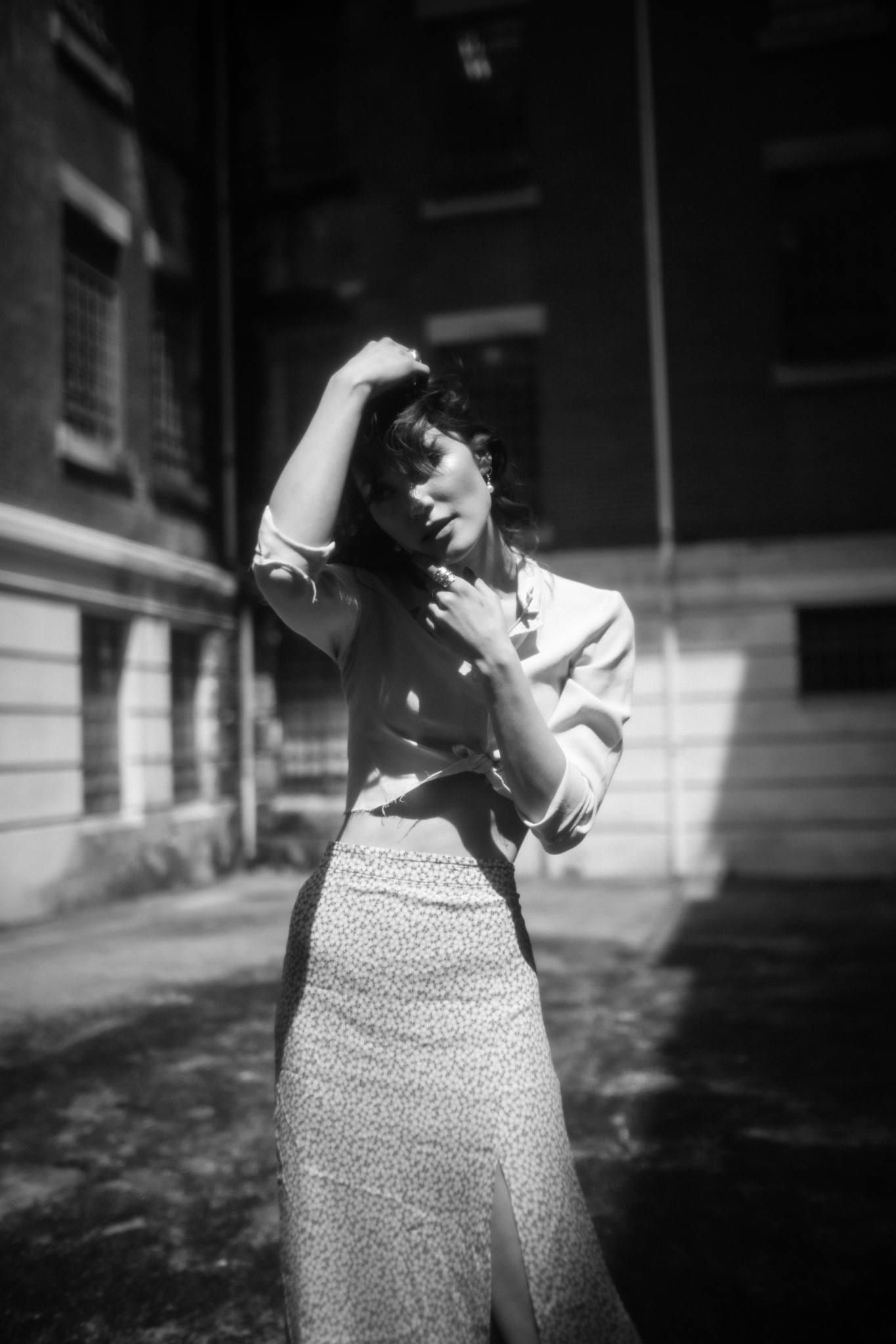 Black-and-white photo of a model with a hand on her head before a brick building