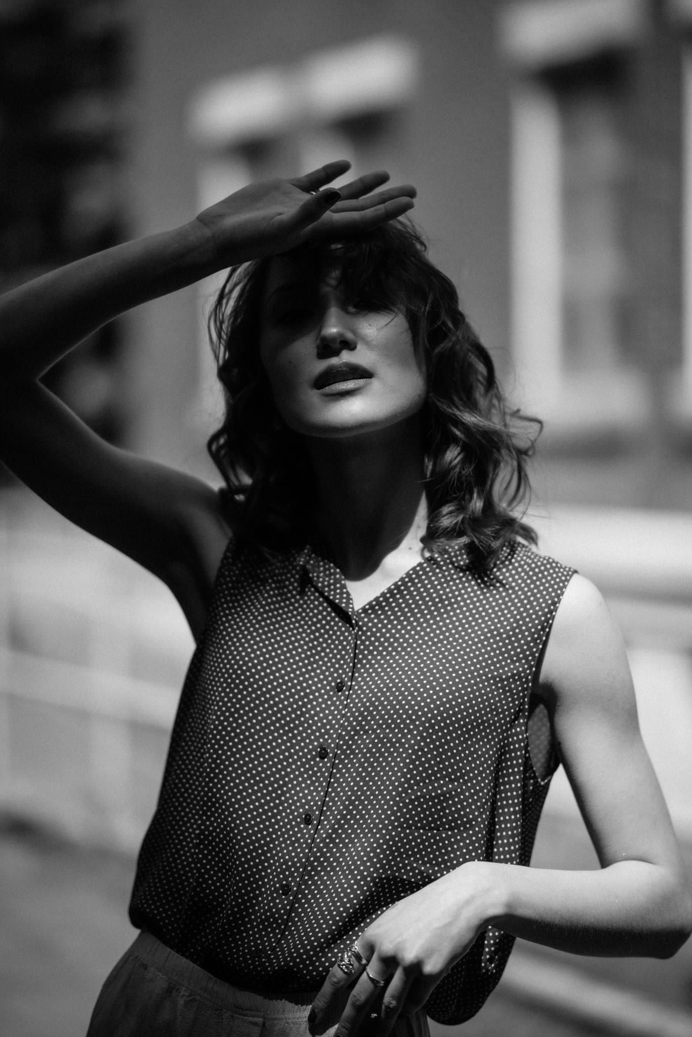 Black-and-white portrait of a model in a knit vest shielding her eyes from the sun