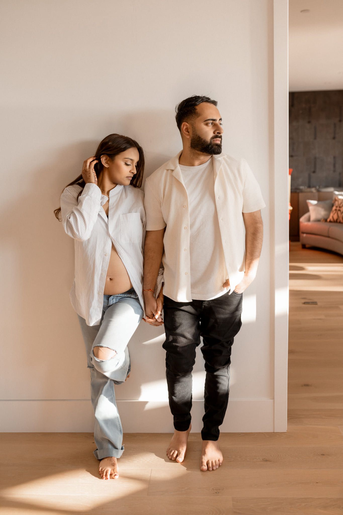 Lifestyle maternity shoot in a sunlit room, expecting couple standing barefoot together