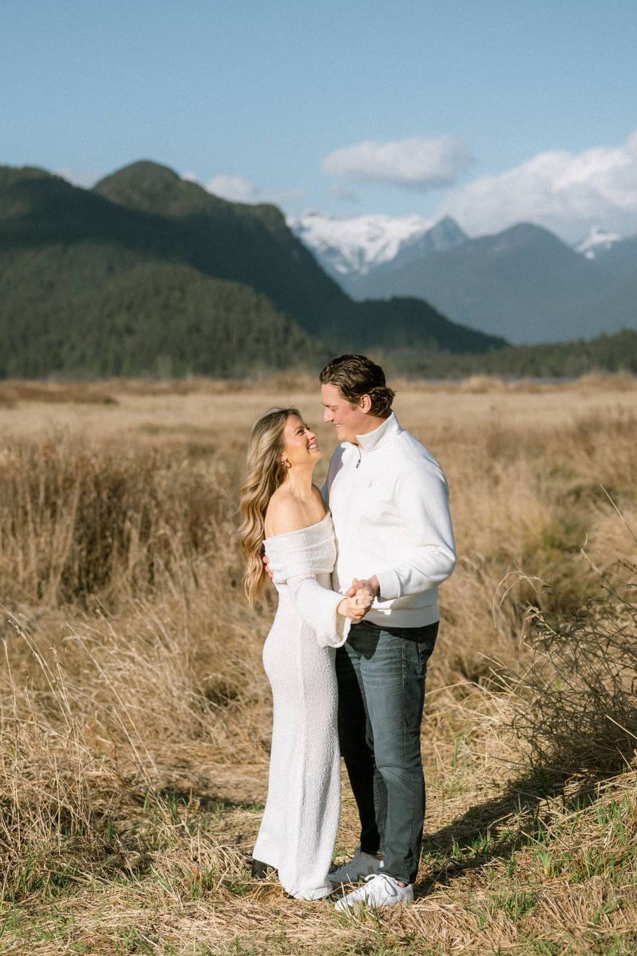 Maternity winter photoshoot, a couple gazes at each other in a golden meadow with snow-capped peaks in the distance