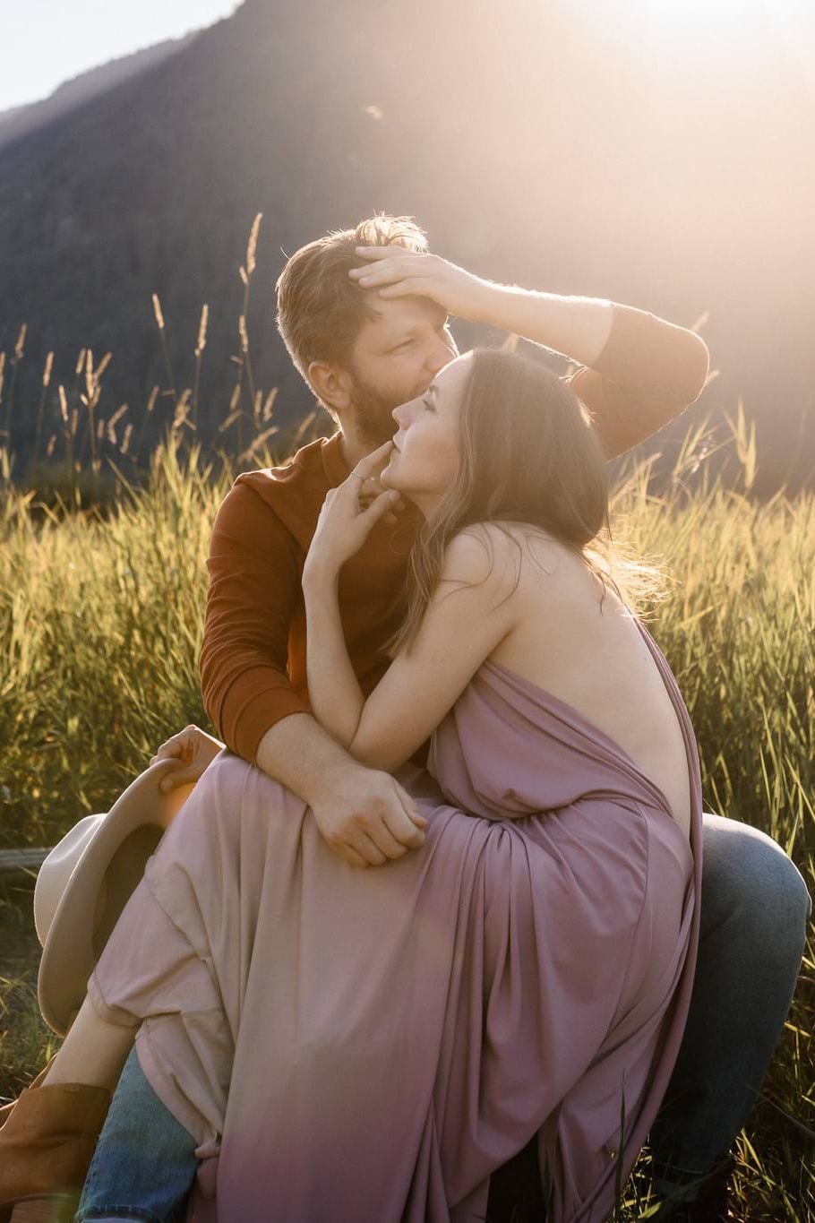 Golden hour engagement photos at sunset below the mountains, couple embracing in golden grass