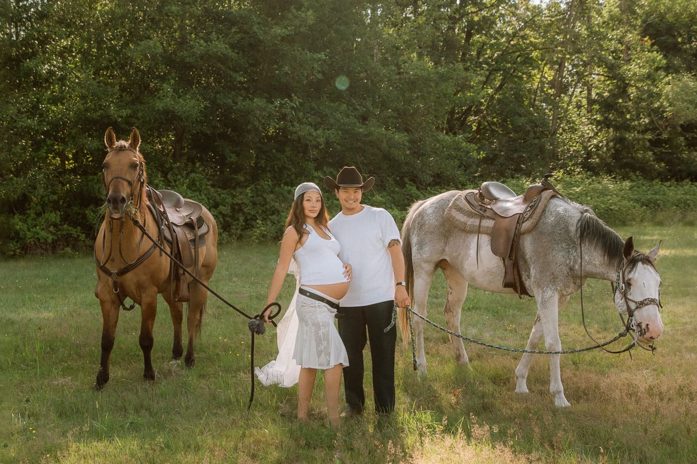 Maternity photos in Coquitlam, expectant couple standing between two horses in a green meadow