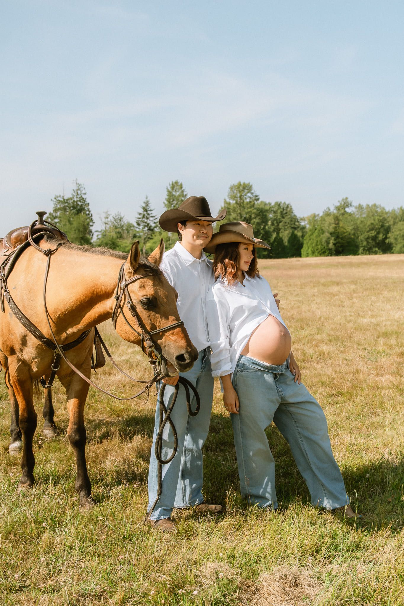 Maternity photos outside in a summer meadow, expectant mother in white with two horses