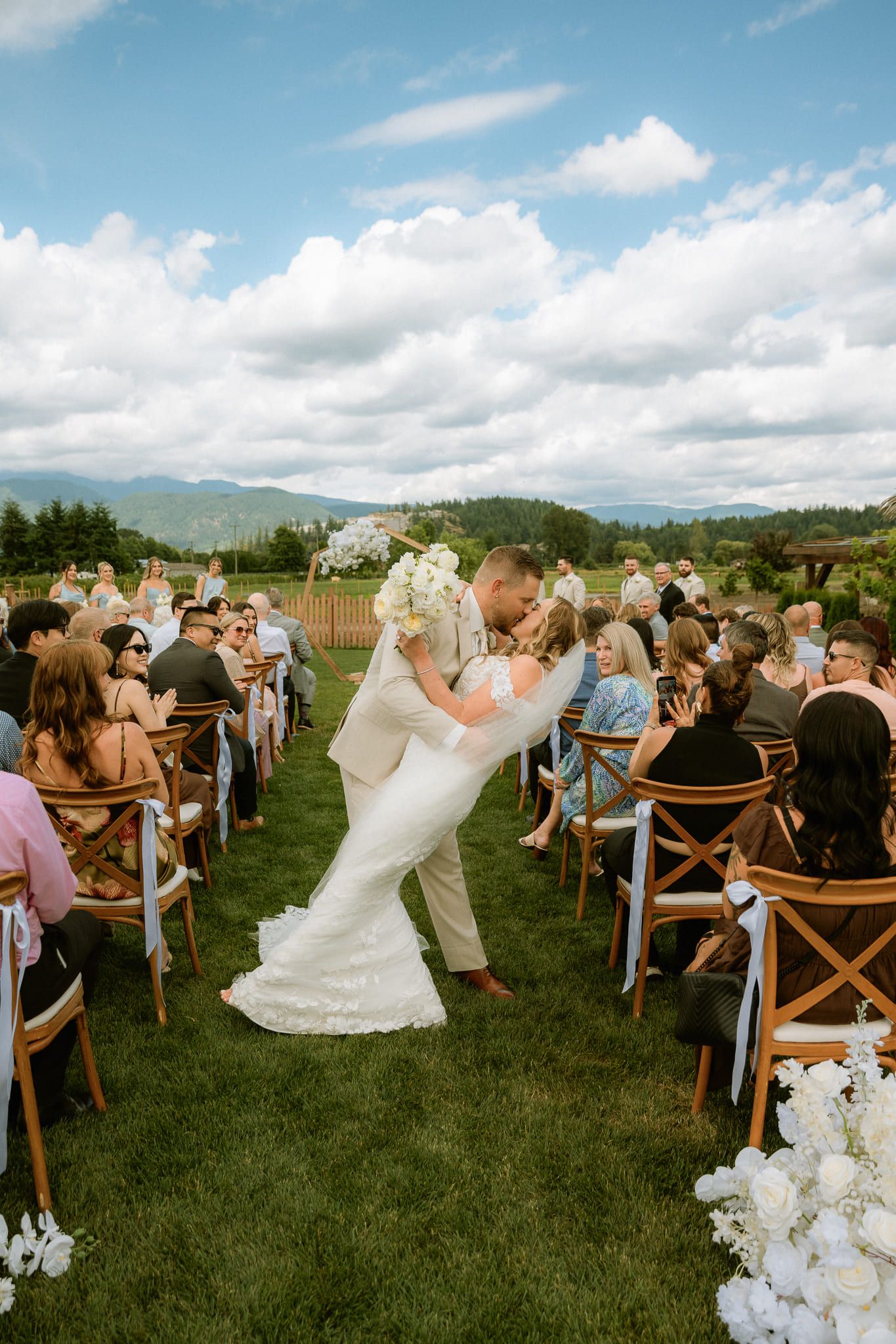 Professional wedding photos in a meadow, bride and groom kissing as they walk up the aisle between guests