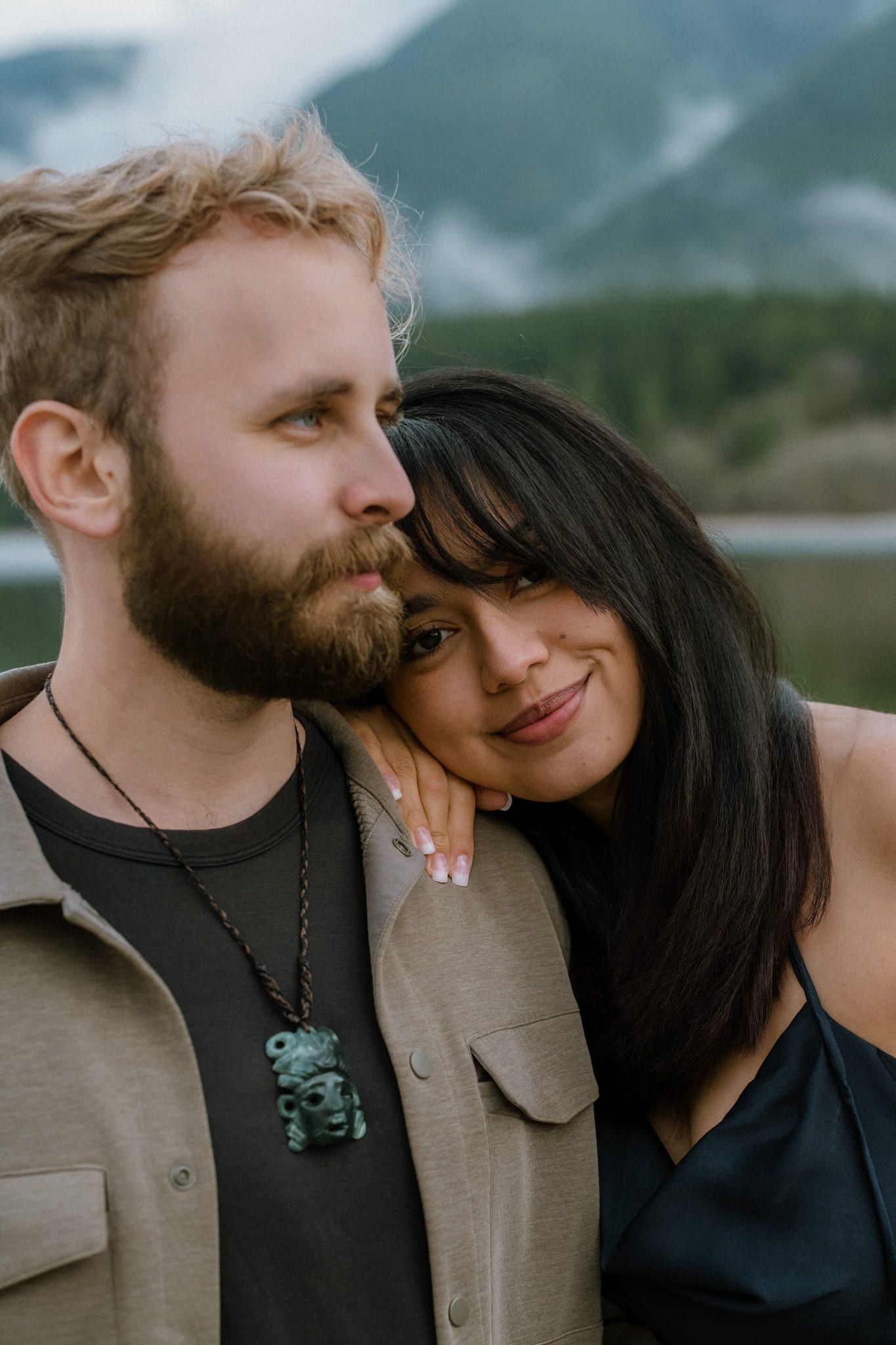 Engagement photos outside below misty mountains, couple cuddling on a lakeshore