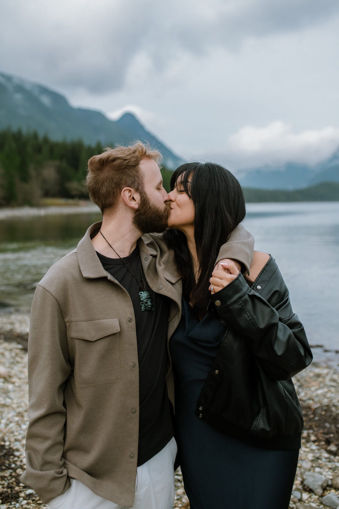 Intimate couple photoshoot below misty mountains, couple cuddling on a lakeshore