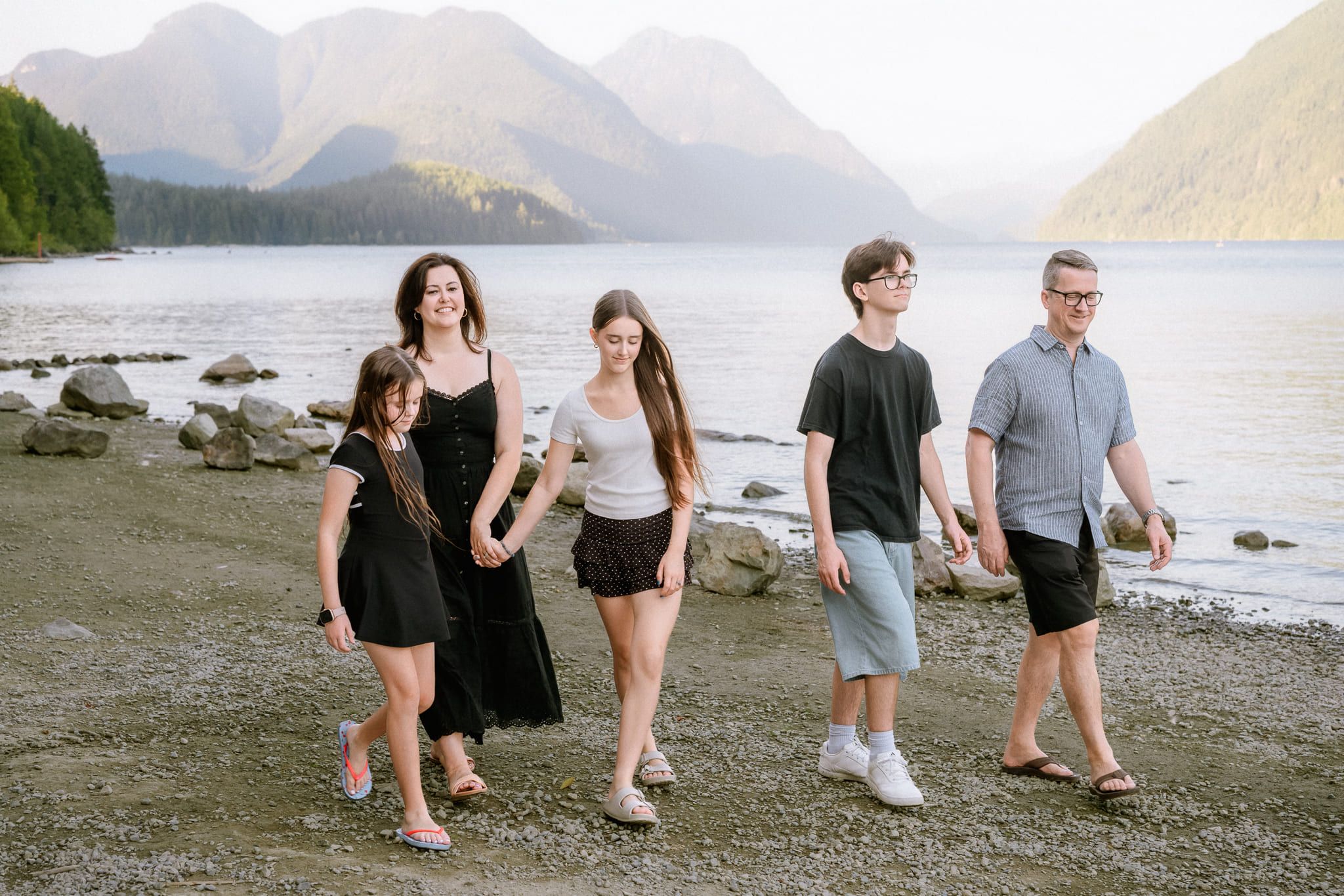 Professional family pictures, family walking together along a lakeshore with mountains behind