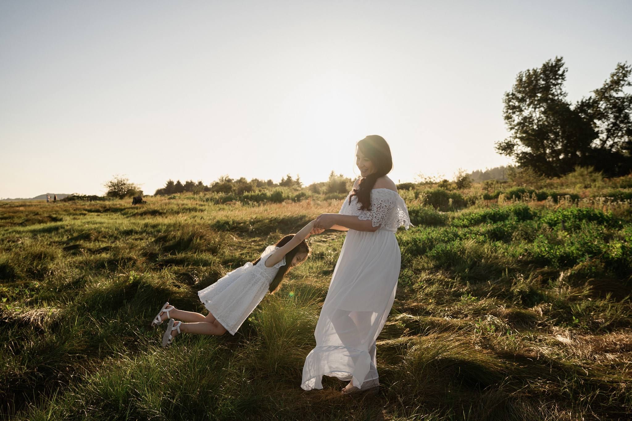 Mother in a white dress swinging her daughter around in a golden meadow