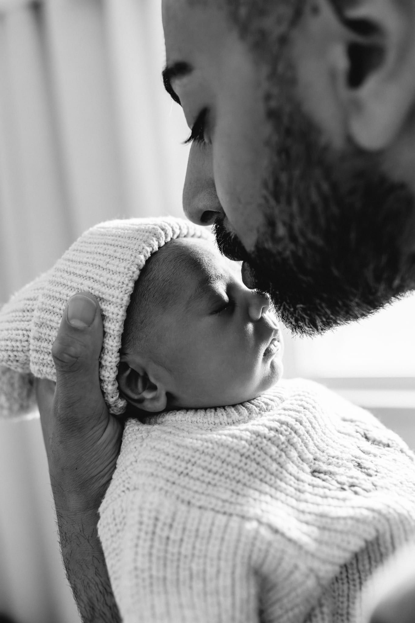 Newborn and dad photos, dad kissing his sleeping newborn's forehead, in black and white