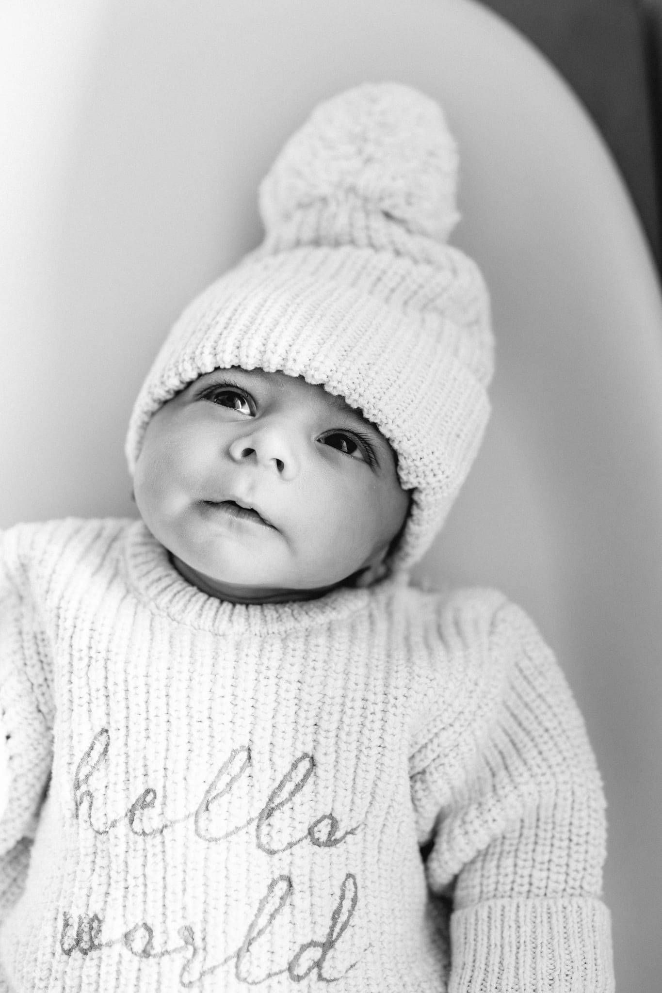 Simple newborn photos, newborn baby in a knitted pom-pom hat and a "hello world" sweater, in black and white
