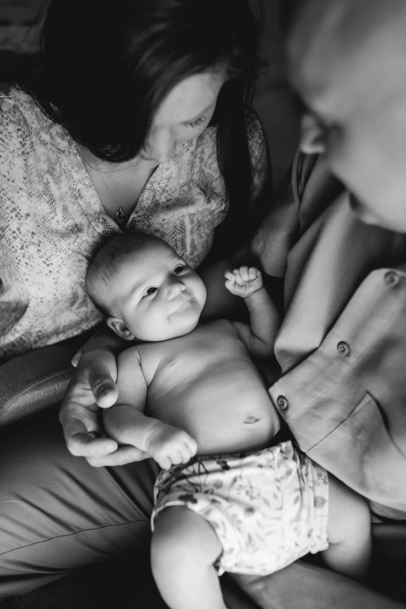 Newborn family photoshoot, newborn lying in his parents' laps, in black and white