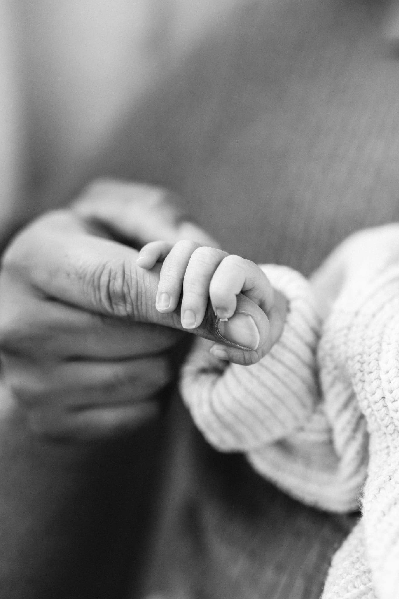 Newborn details photography, close-up of a newborn's hand around a parent's finger, in black and white