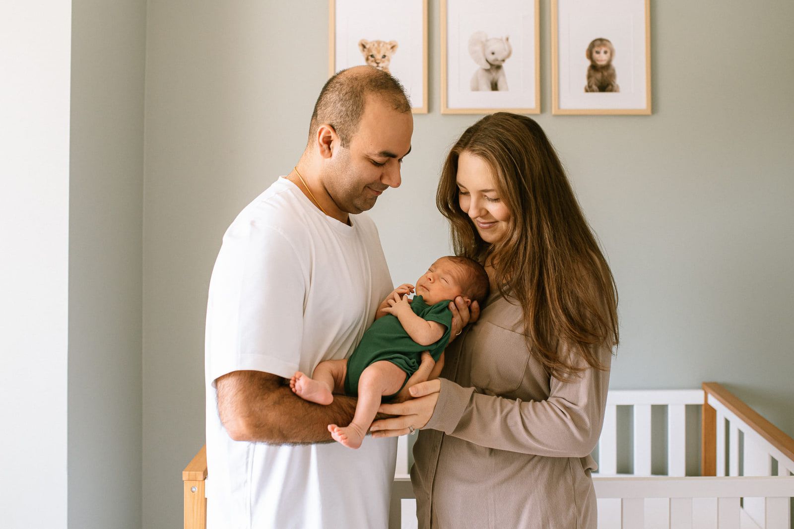 Lifestyle newborn photography, newborn boy in a green bodysuit with his parents in their nursery