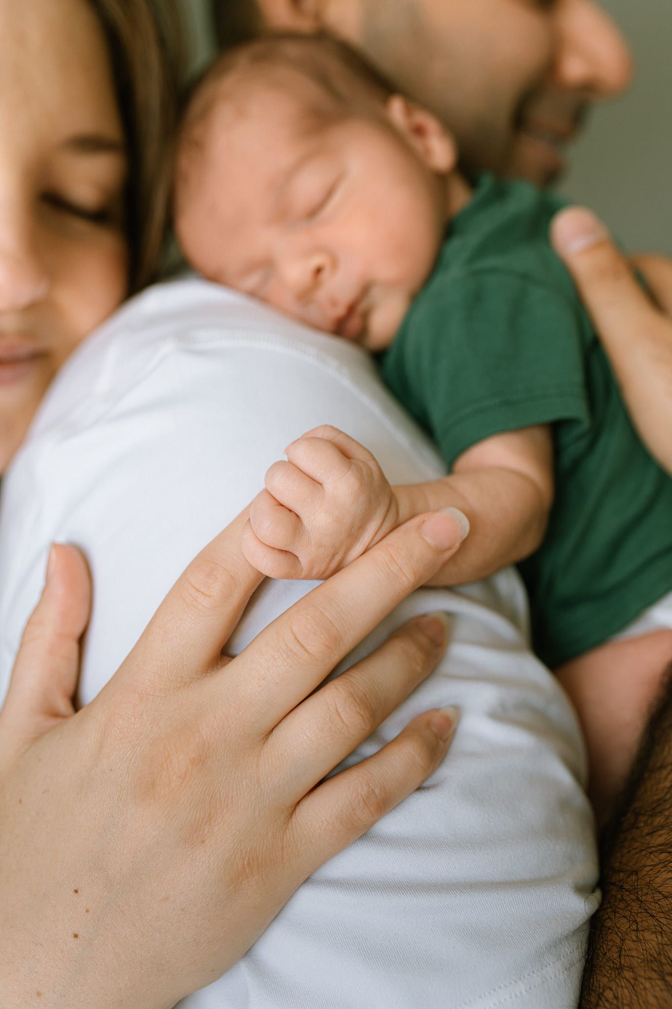 Newborn photography at home, newborn boy in a green bodysuit with his parents in their nursery