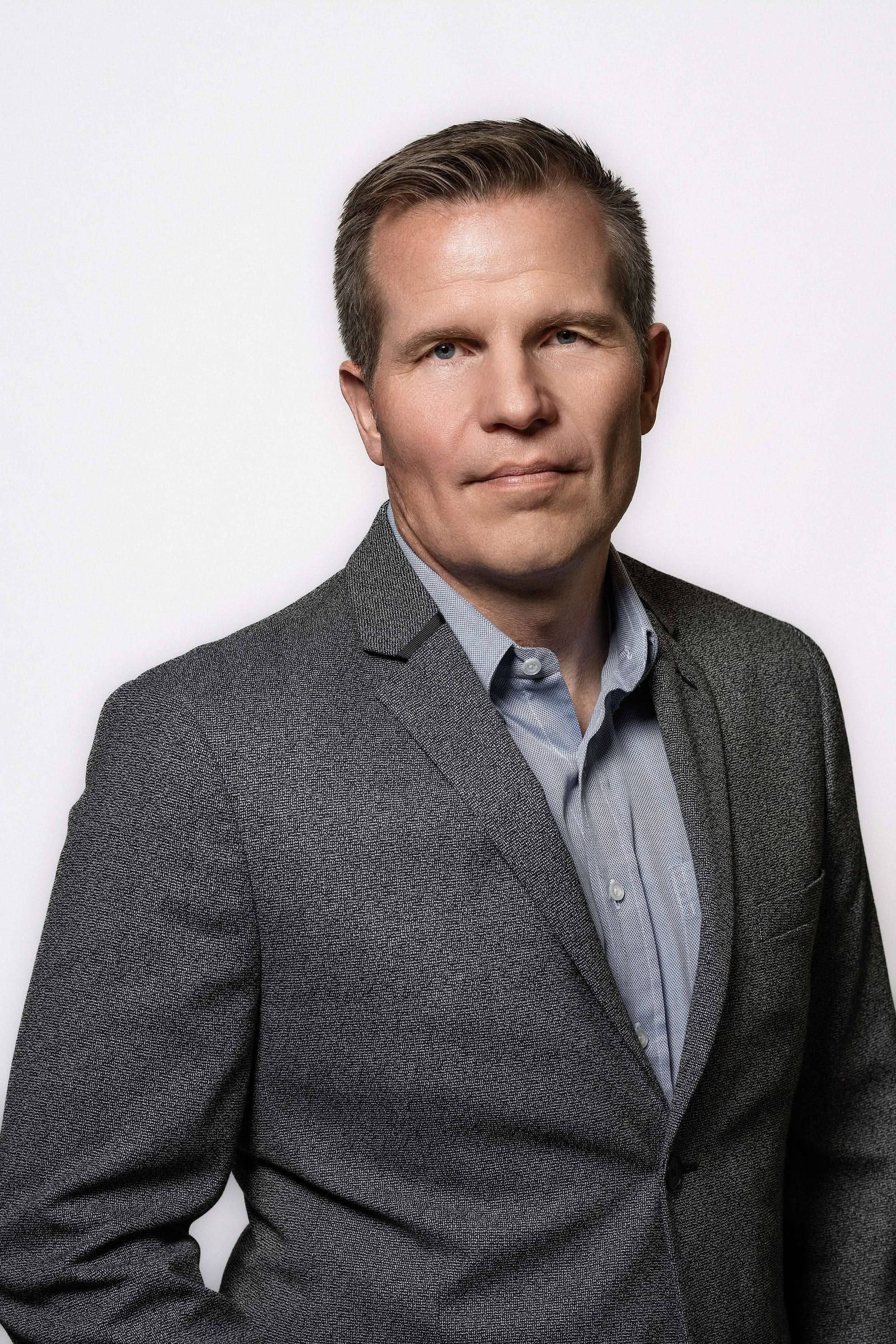 Man in a grey blazer and blue shirt on a white backdrop