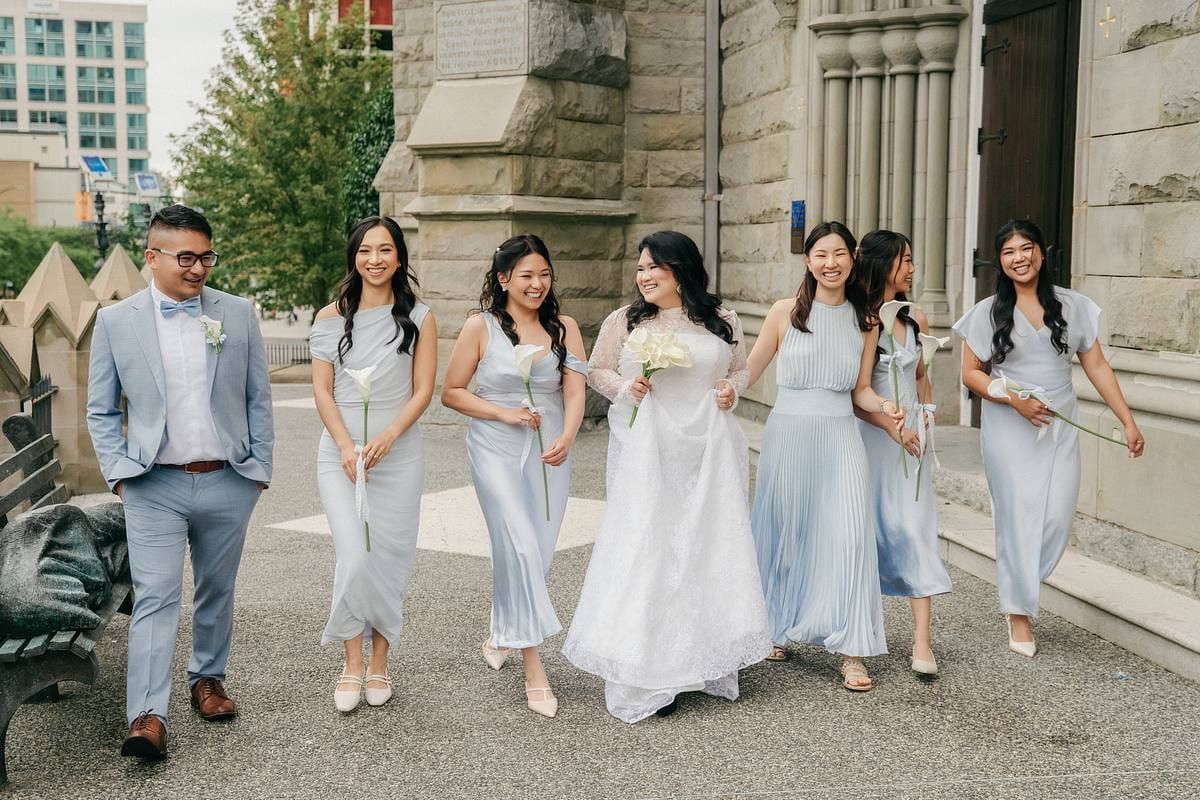 Groom photos, groom and bridesmaids in soft blue walking outside a stone heritage building